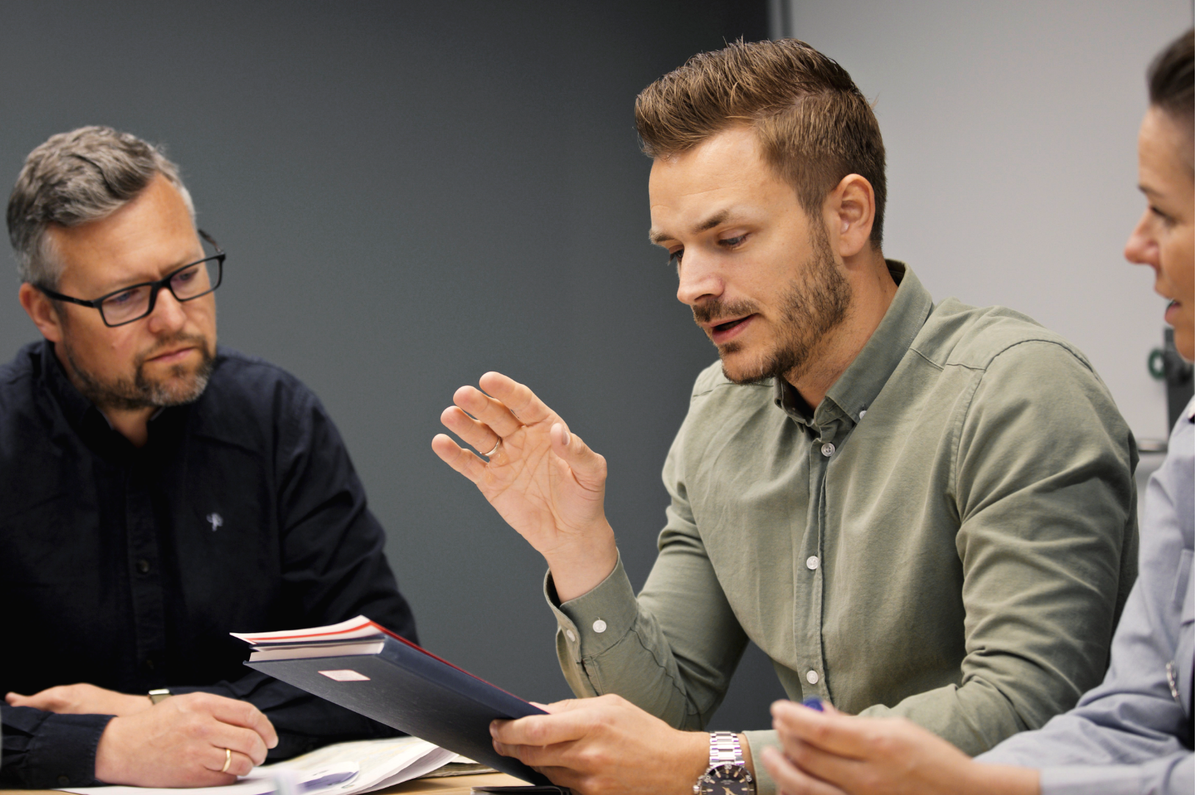 To menn og en kvinne sitter rundt et bord og diskuterer.