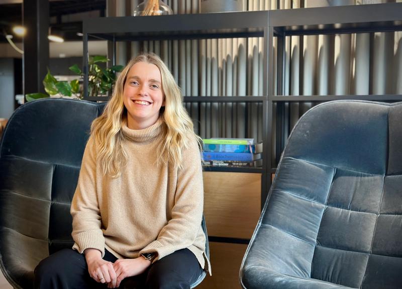Dame med lyst langt hår sitter i en blå stol i kontorlandskap