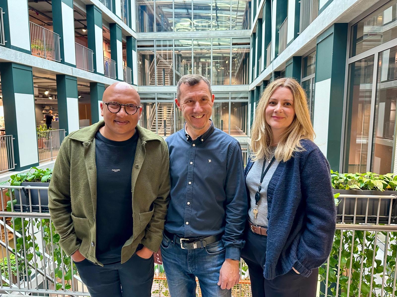 To menn og en kvinne står innendørs i en stor bygning