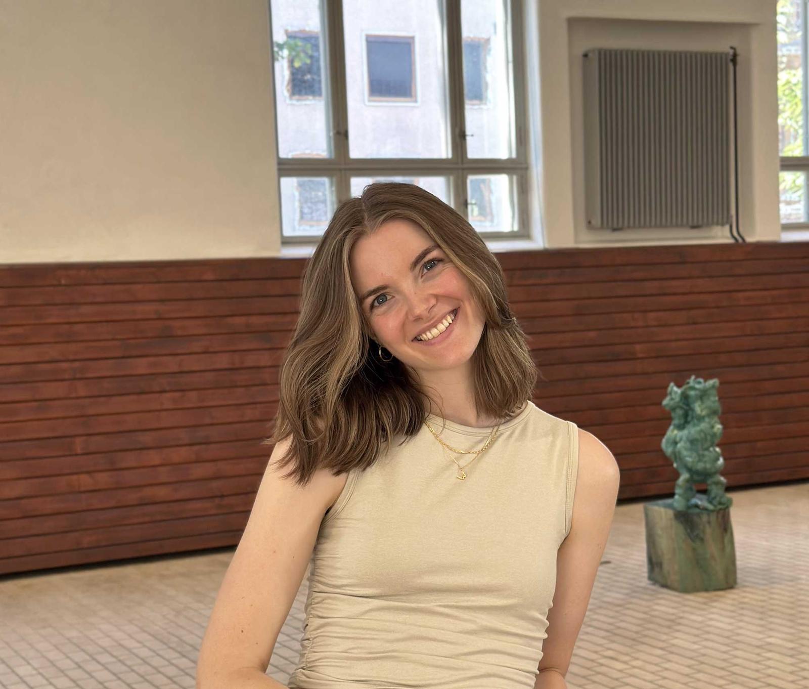 Dame med langt hår og lys topp poserer for kamera innendørs med hodet på skakke.