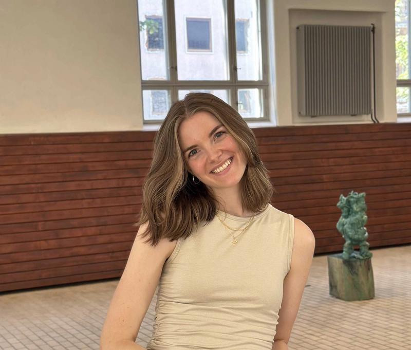 Dame med langt hår og lys topp poserer for kamera innendørs med hodet på skakke.