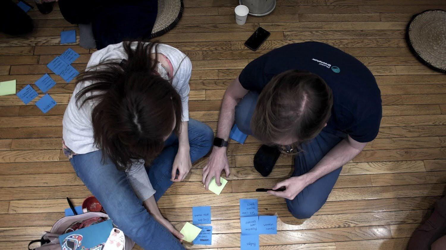 To mennesker sitter på gulvet med masse post-it-lapper