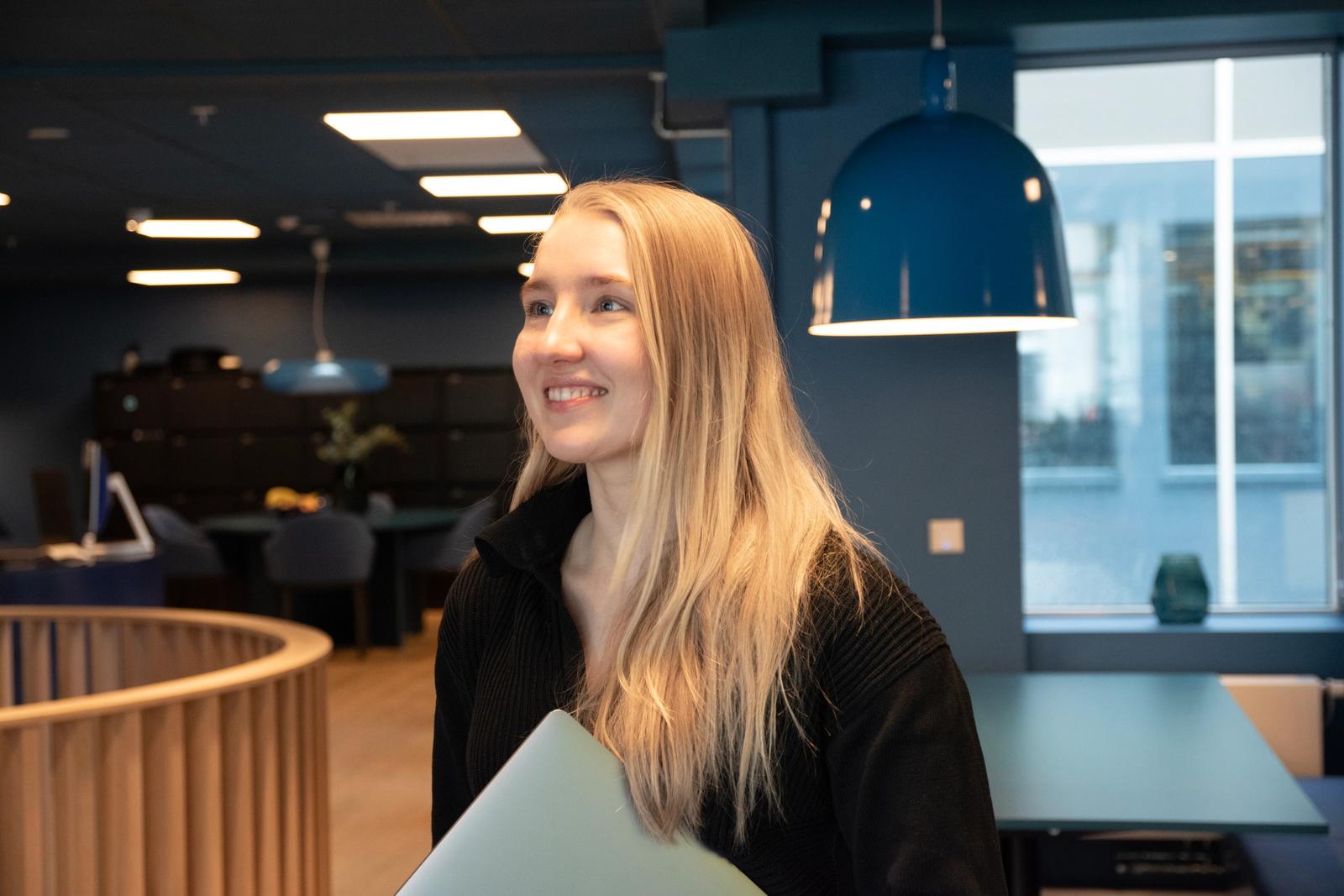 Åse Lilly Salamonsen ser sidelengs i blått kontorlandskap. Hun har langt, stritt hår i gyldende toner.