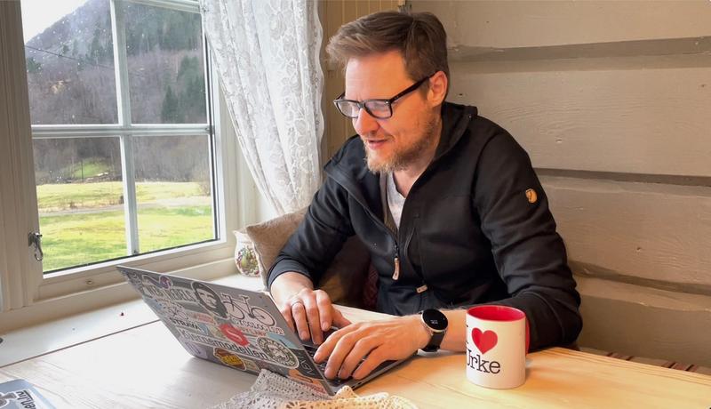 Are sitter med laptopen ved kjøkkenbordet.