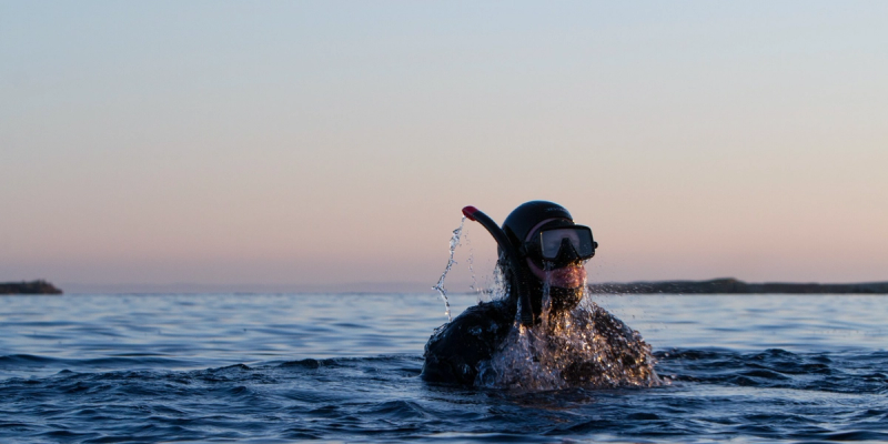 Landskapsbilde av sjøen, hvor mann i dykkerutstyr akkurat har kommet over overflaten på vannet etter dykk.
