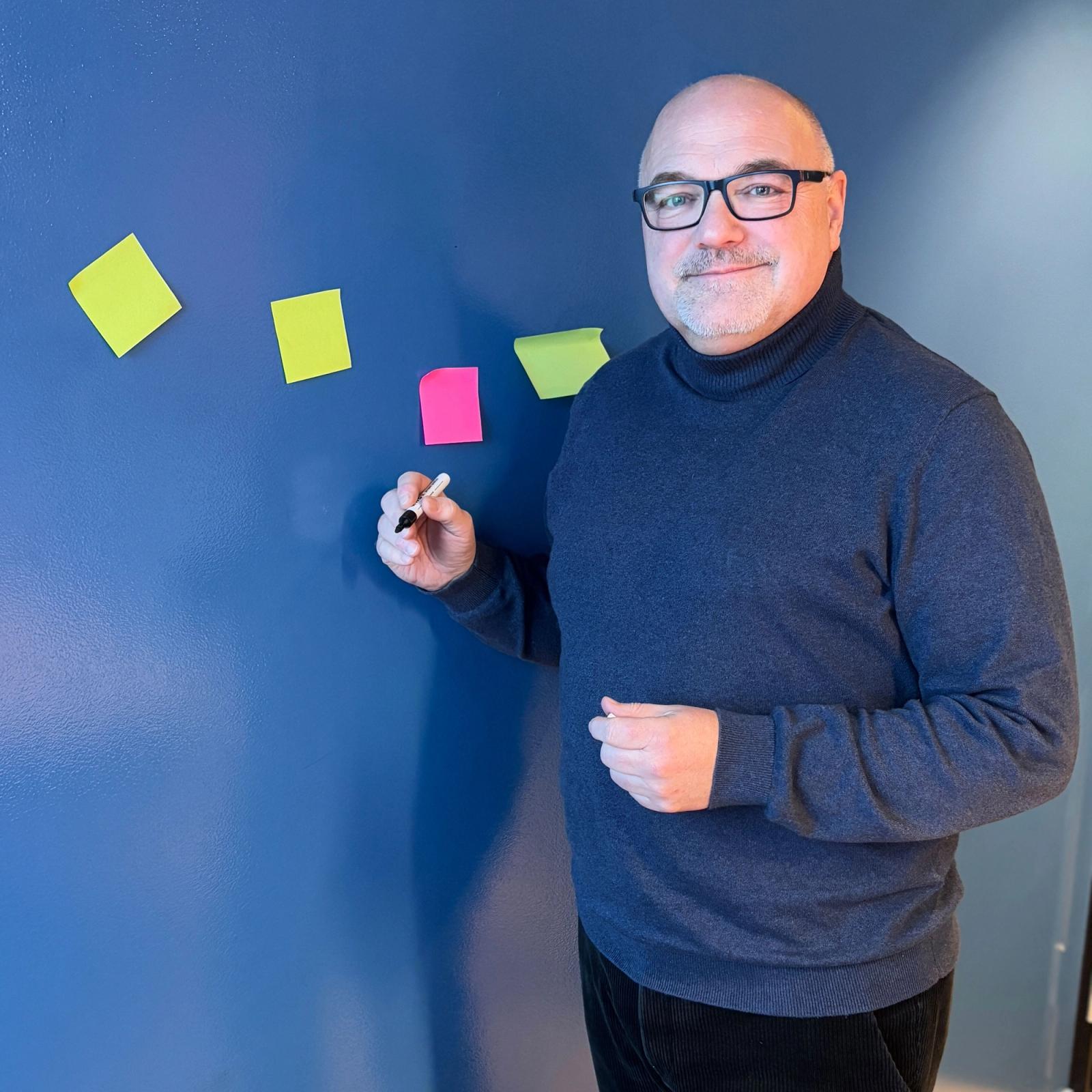 Mann med briller står ved en vegg og skriver på post-it-lapper