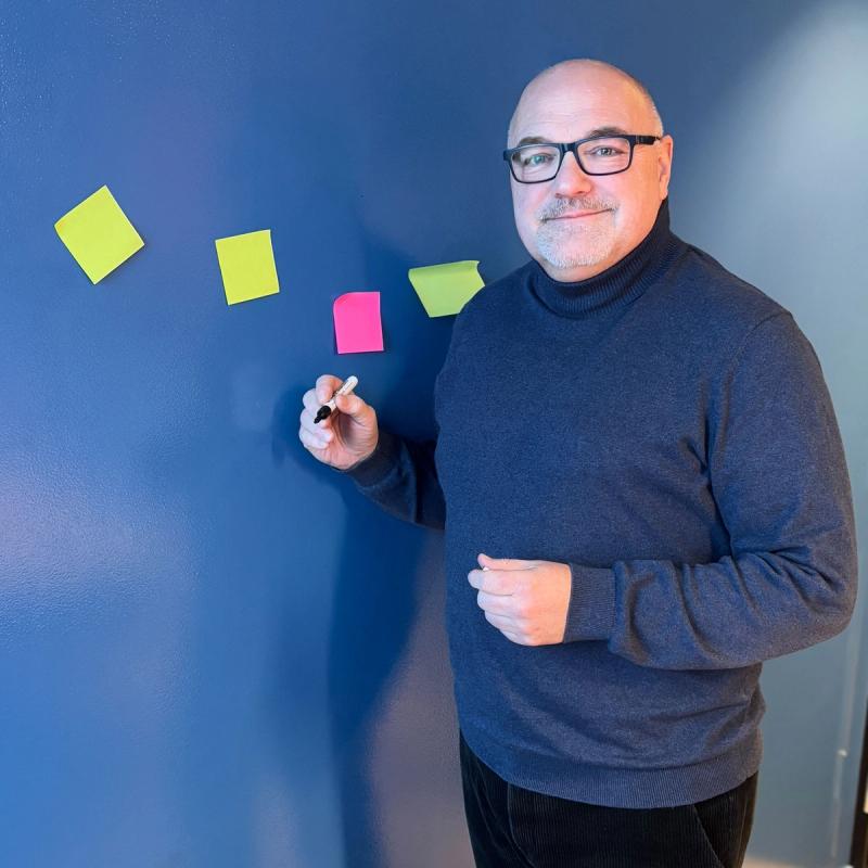 Mann med briller står ved en vegg og skriver på post-it-lapper