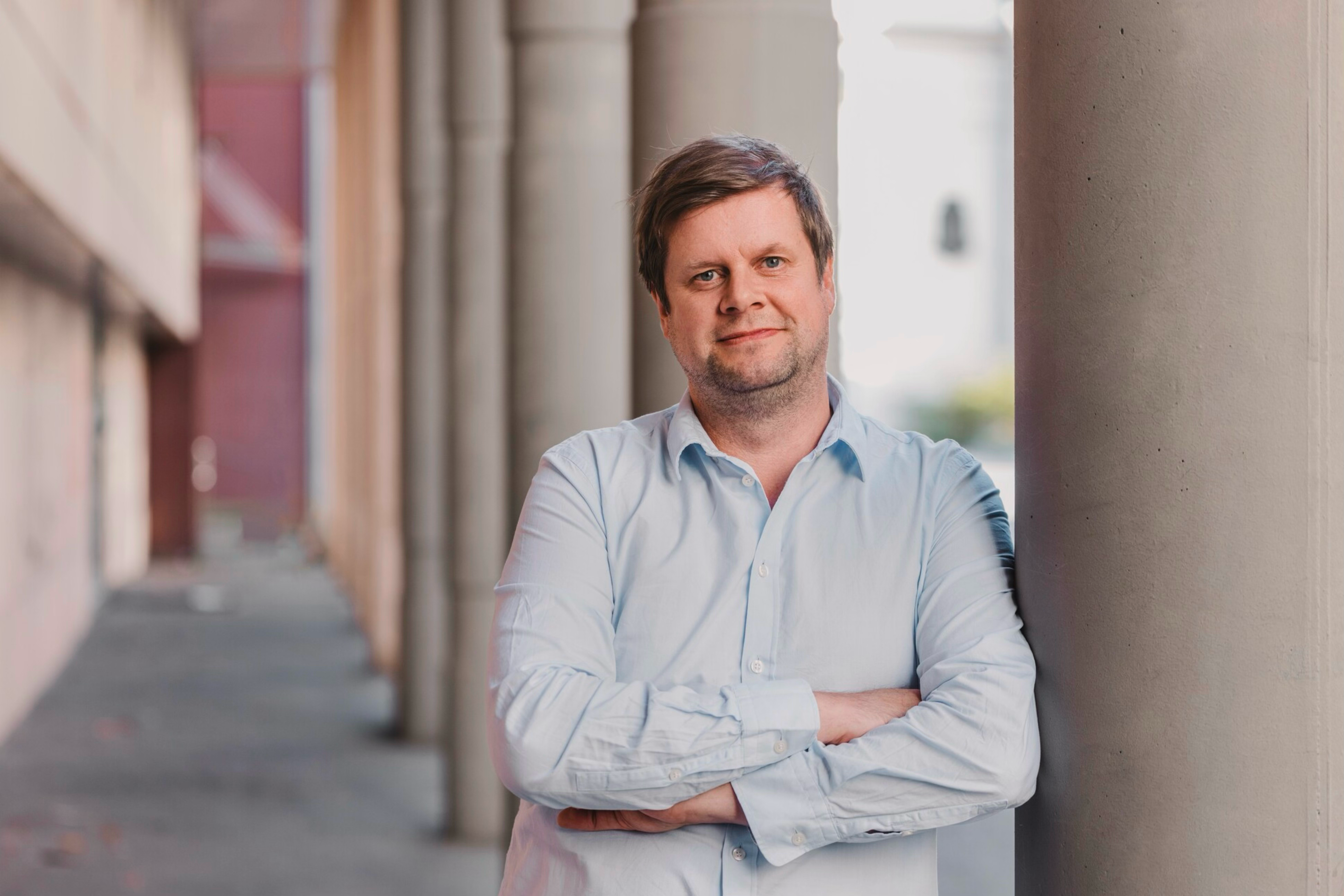 Mann i skjorte står utendørs og lener seg inntil en stor stolpe.