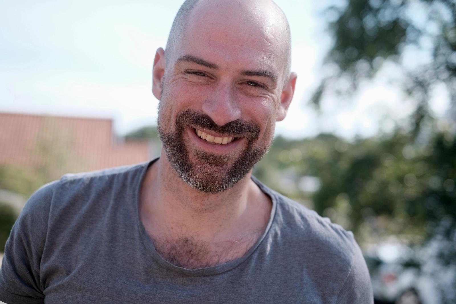 Smilende mann med skjegg uten hår på hodet.