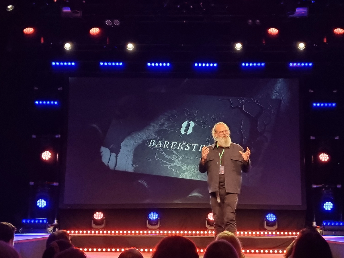 Mann står på scenen og gestikulerer. Foto