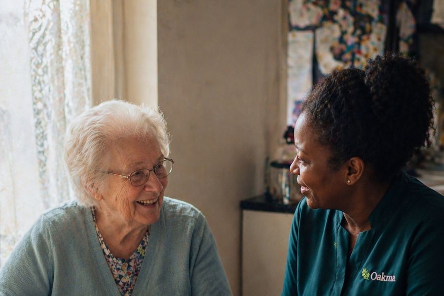 An Oakma carer chatting with an older woman over a pot of tea at her kitchen table