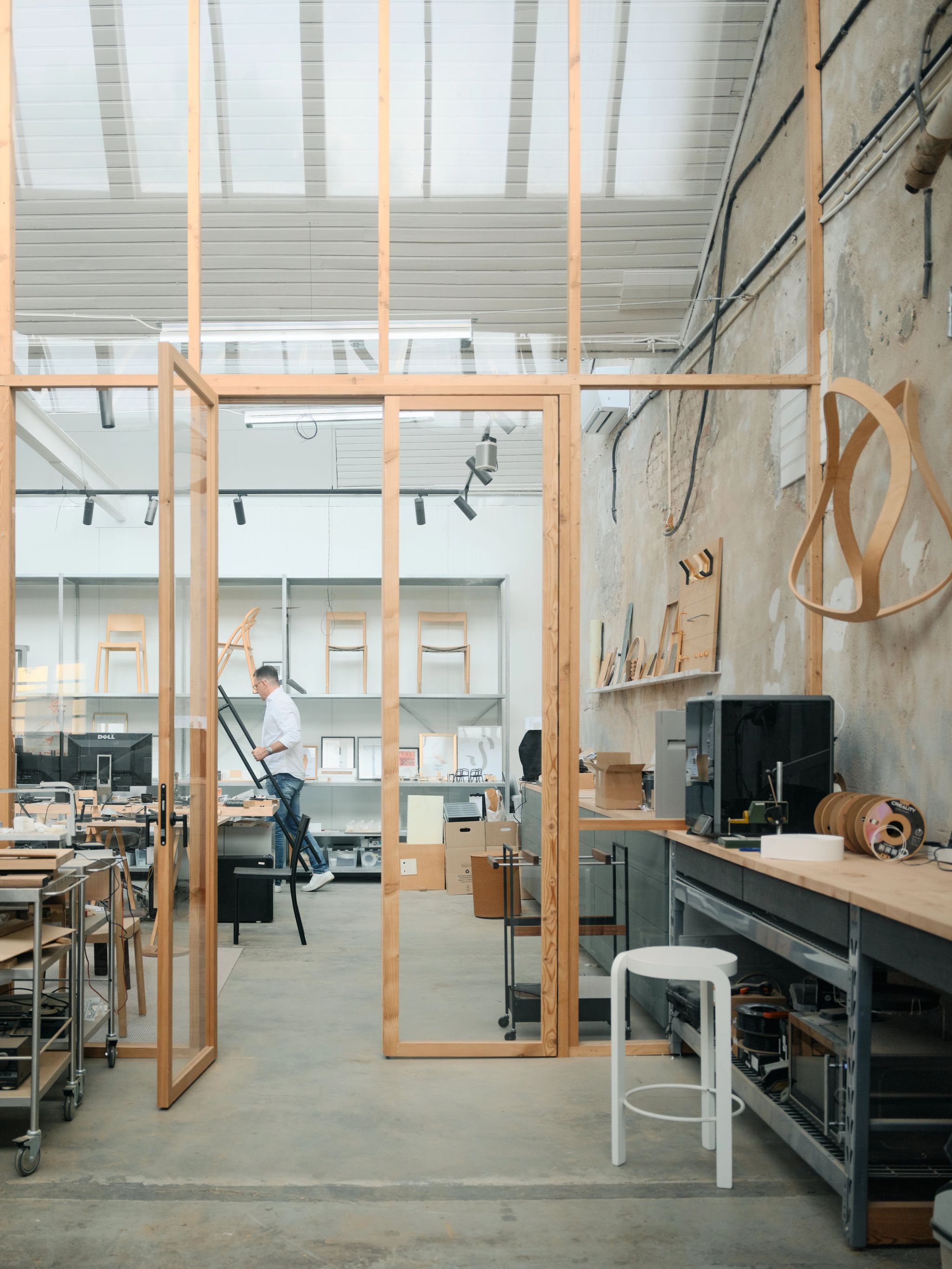 Interior view of a bright design studio with wooden furniture, shelves, and a person working inside.