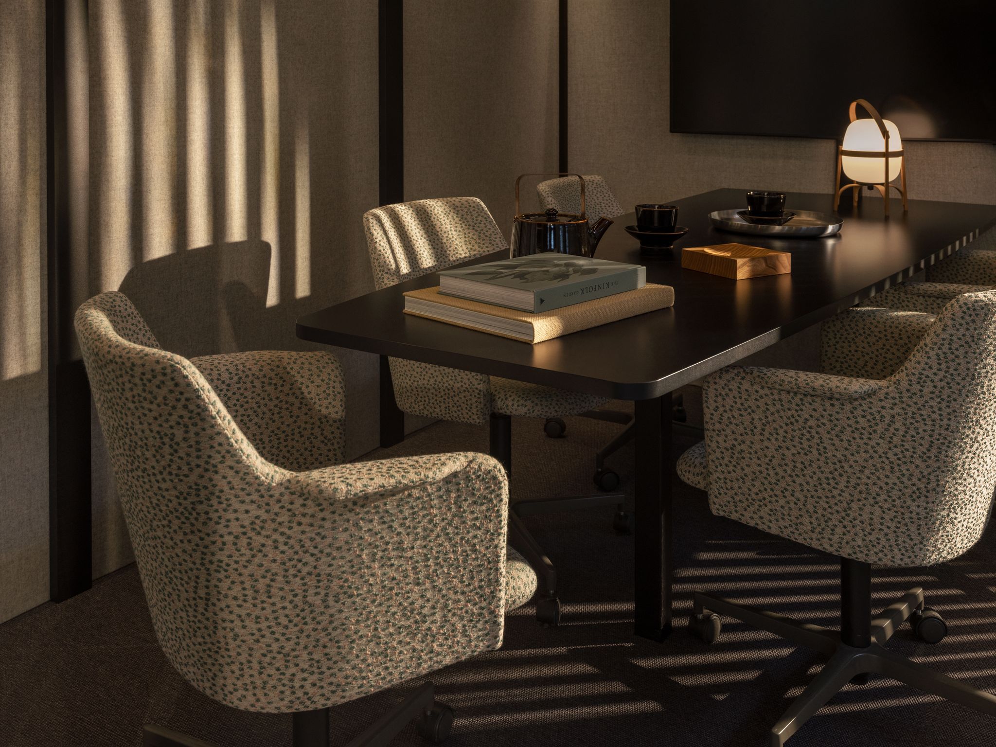 Zen Pod Meeting room with patterned swivel chairs, a black table holding books, a teapot, cups, and a small lamp.