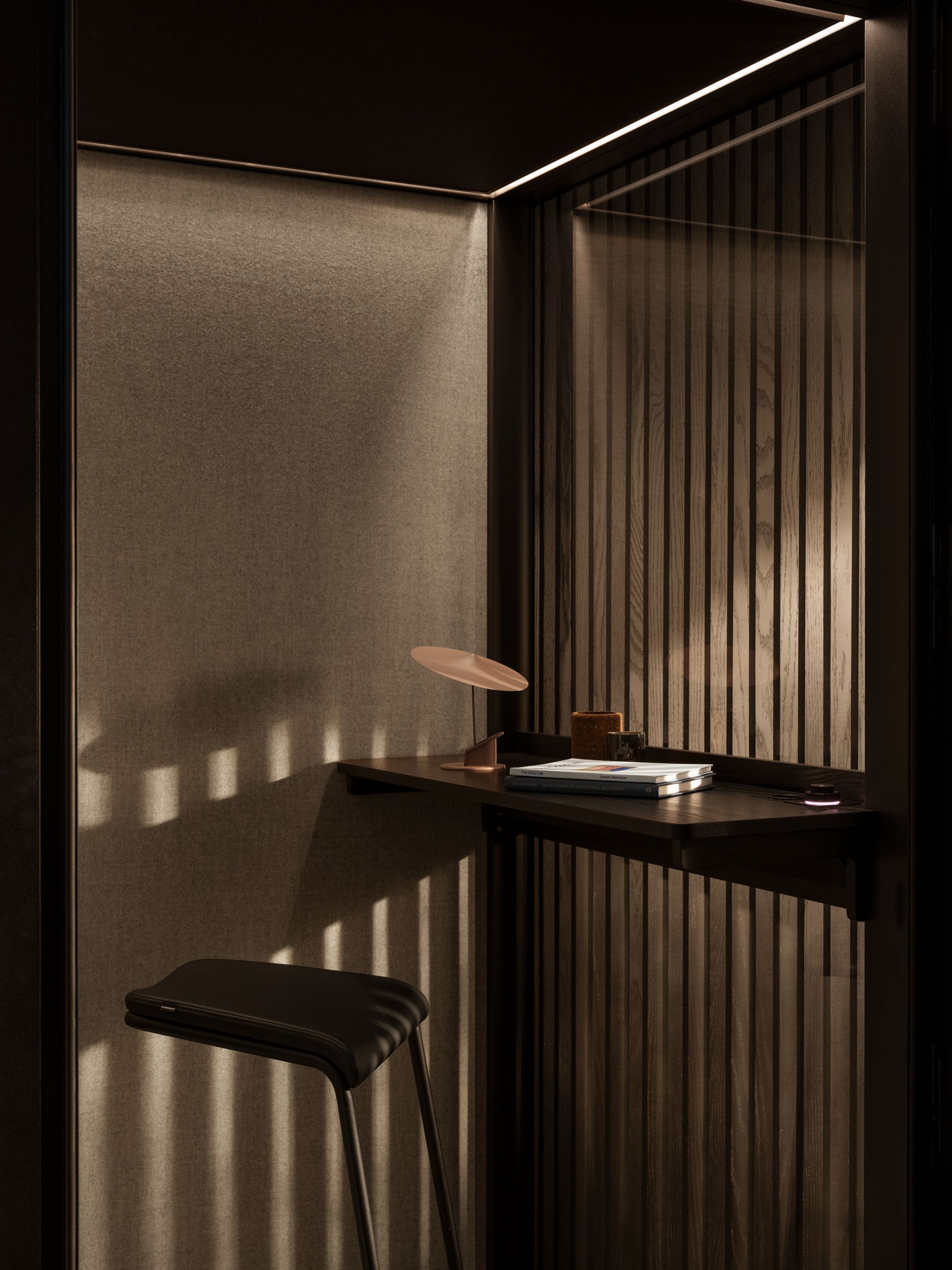 Small workspace with a dark stool, wooden desk, books, and a modern lamp inside a Zen Pod with soft lighting.