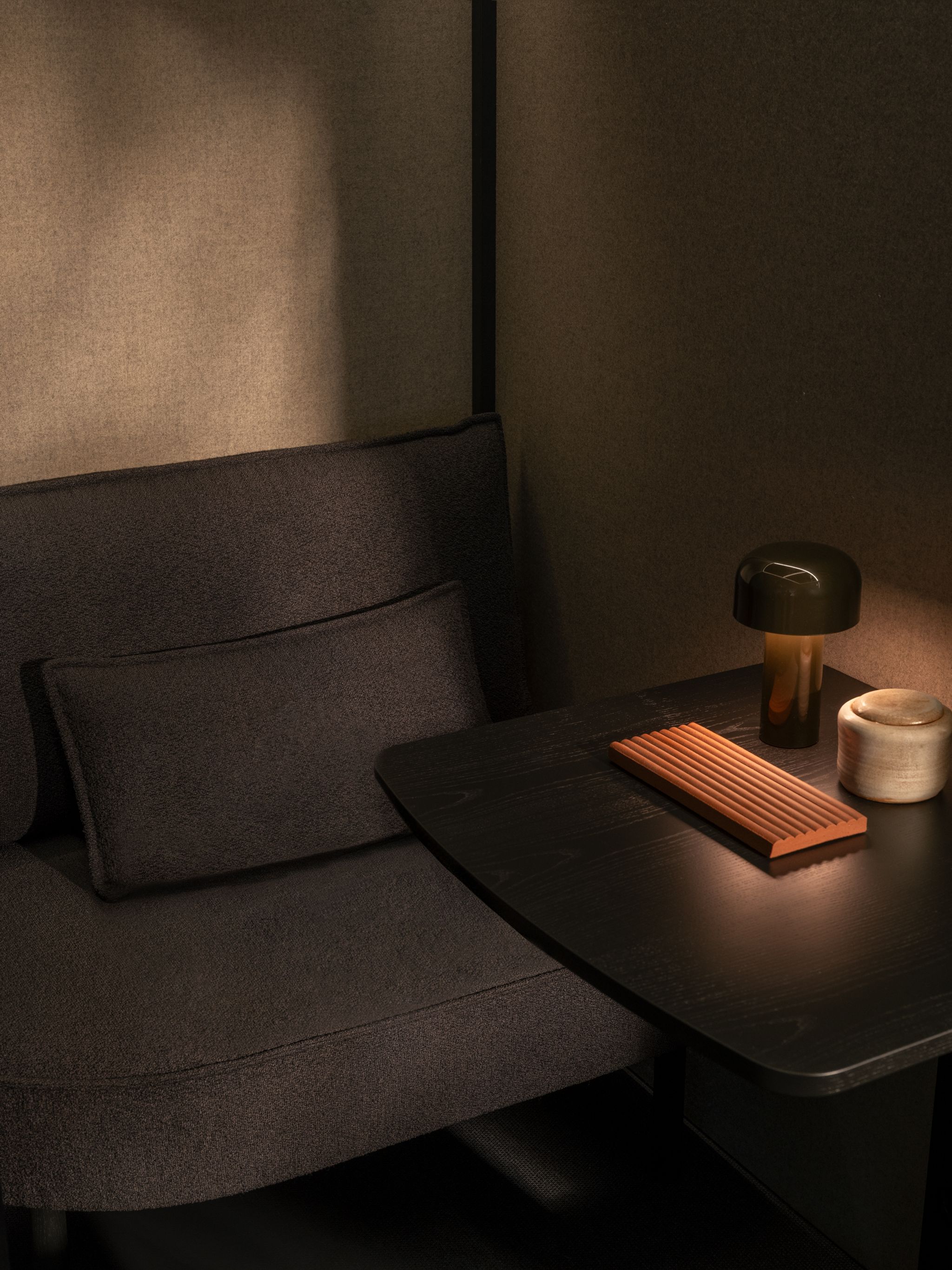 Dark fabric Zen Pod seating with a black table holding a small lamp, a ribbed wooden object, and a ceramic container.