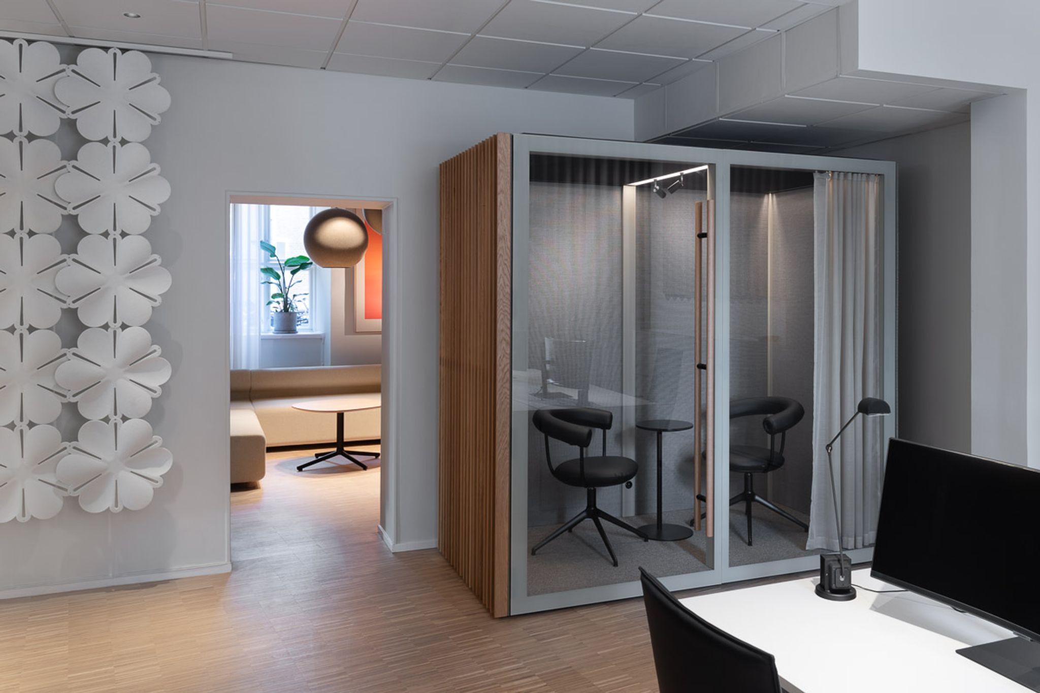 Modern office space with a Zen Pod featuring two black chairs and a small table, adjacent to a lounge area with a beige sofa.