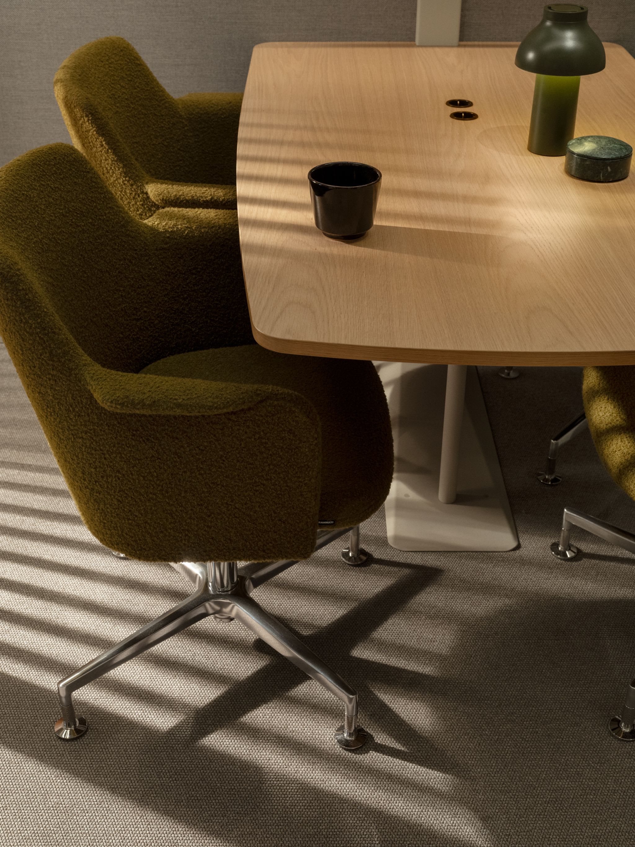 Zen Pod Olive green upholstered office chairs around a light wood table with a black cup and green lamp.