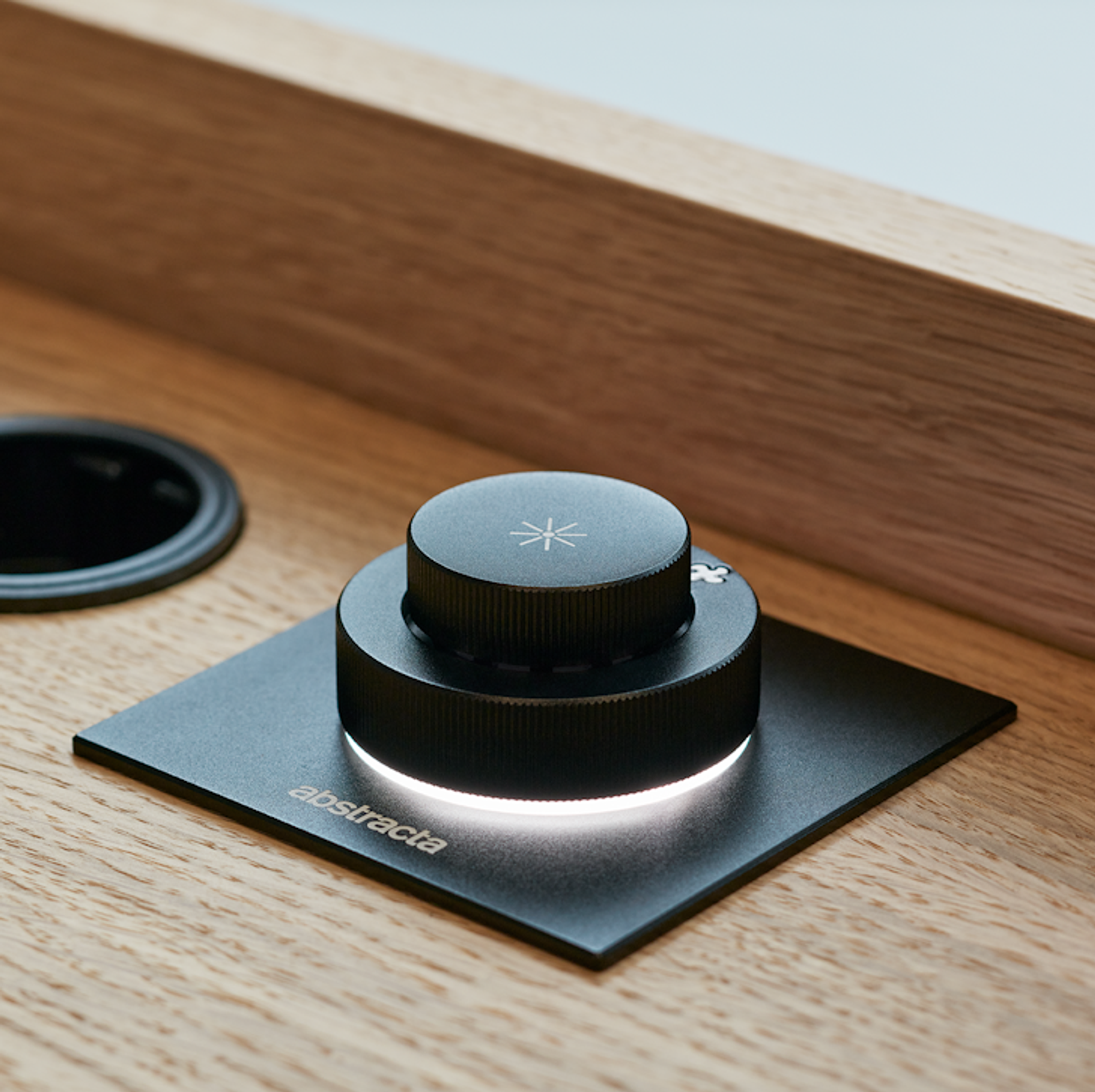 Black Abstracta control knob with illuminated ring on wooden surface near cable port.