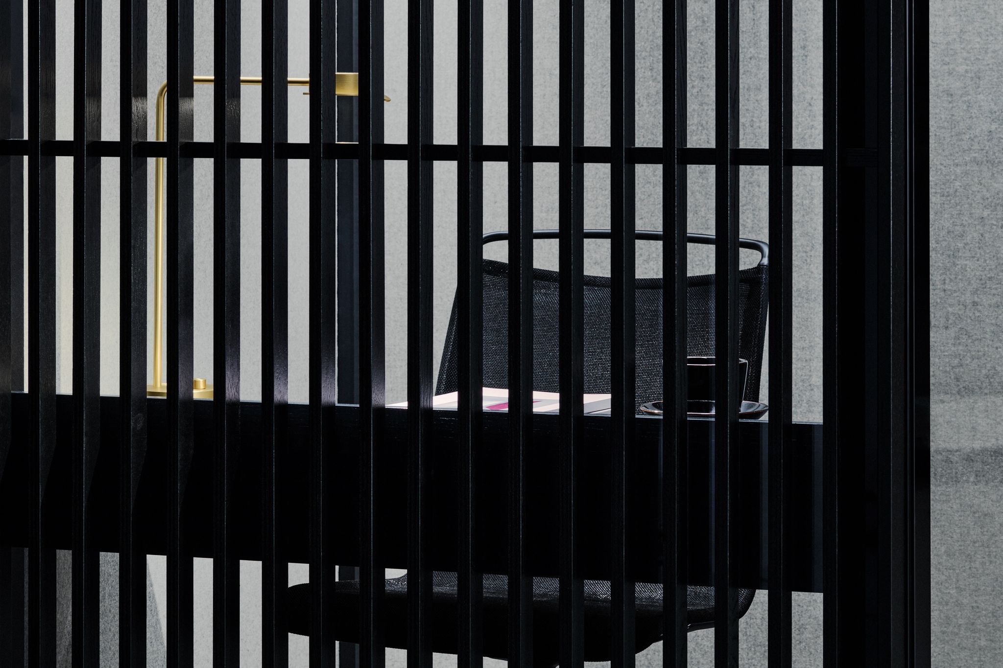 Small dark Zen Pod with chair, desk, and lamp behind slats
