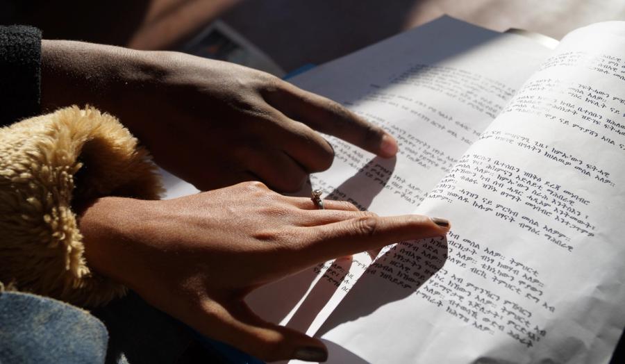 Two hands pointing to a text in a human rights document in Eritrean language