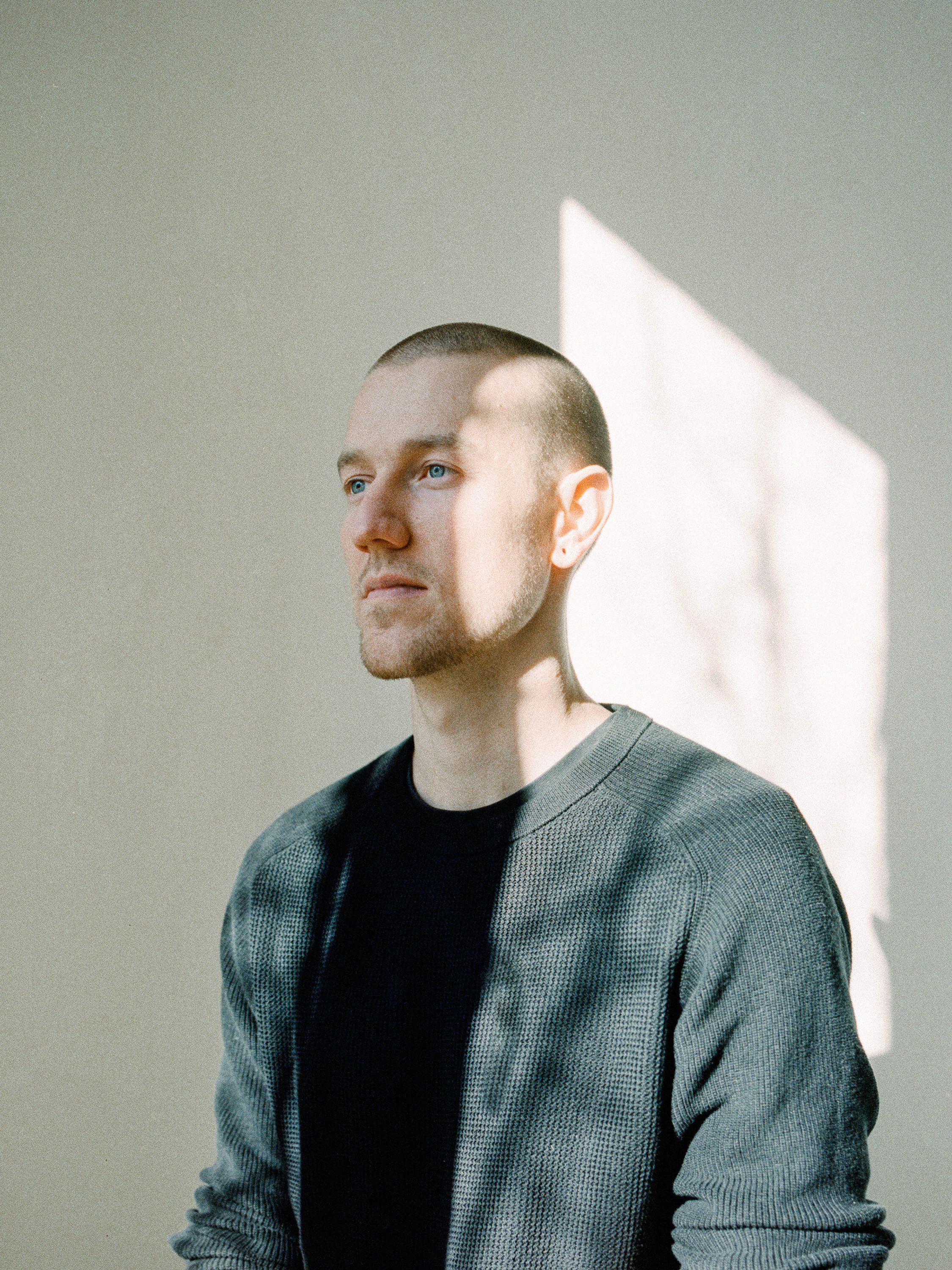 Manuel Lorenz portrait in black sweater in front of gray concrete wall