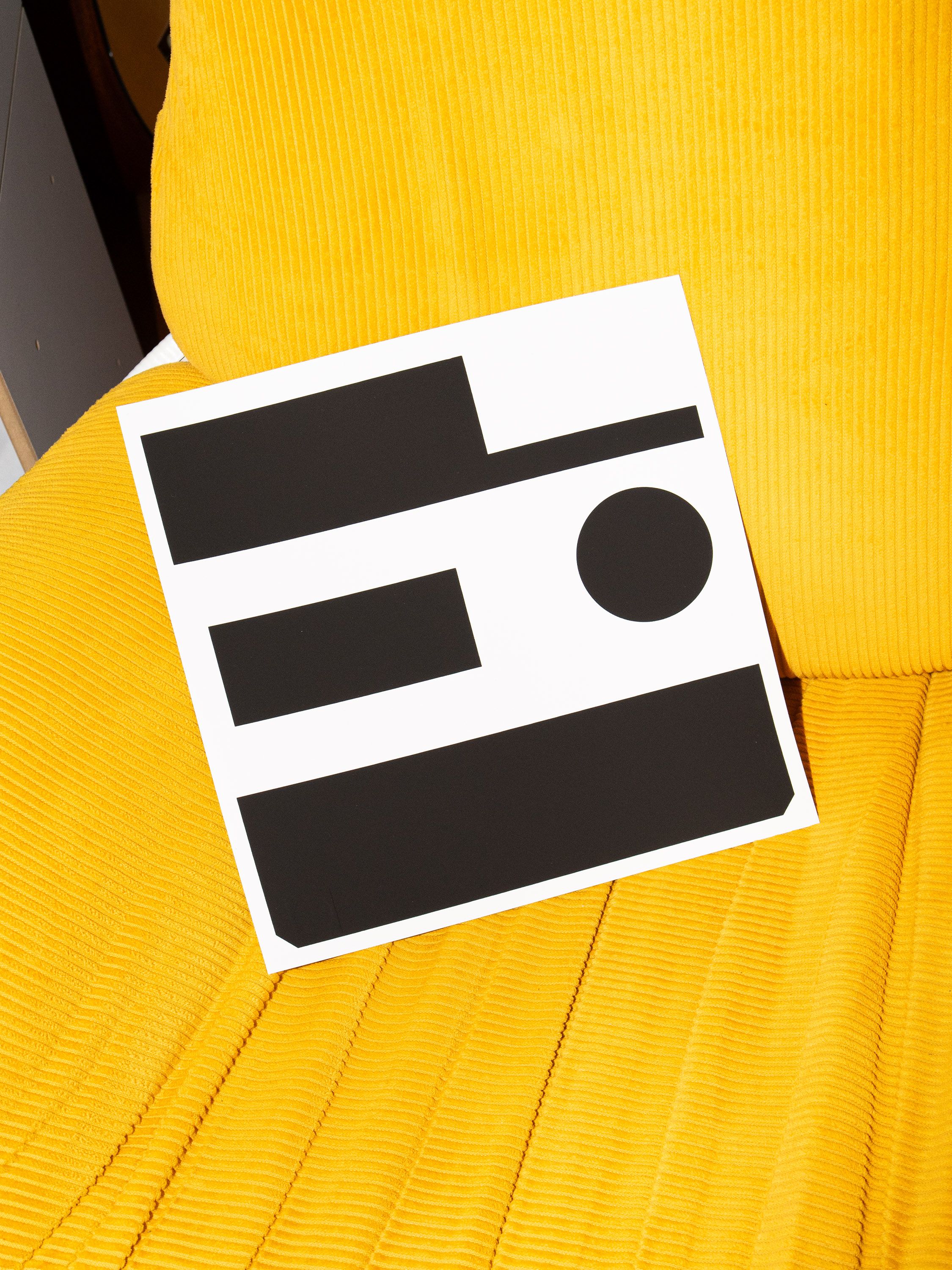 Black-and-white screen print on a yellow chair showing abstract geometric shapes based on a mailbox detail