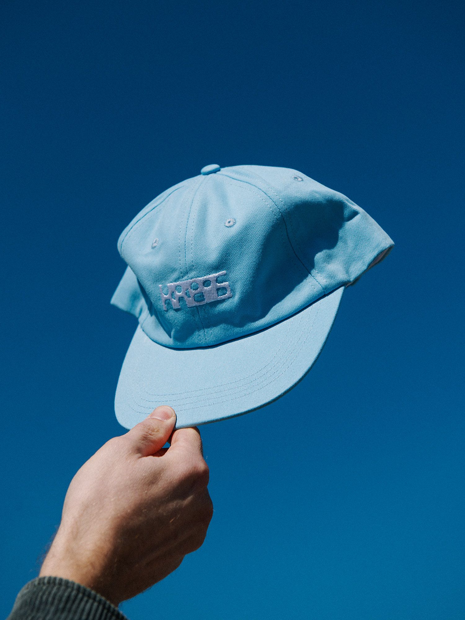Blue cap held up against the sky with white geometric lettering