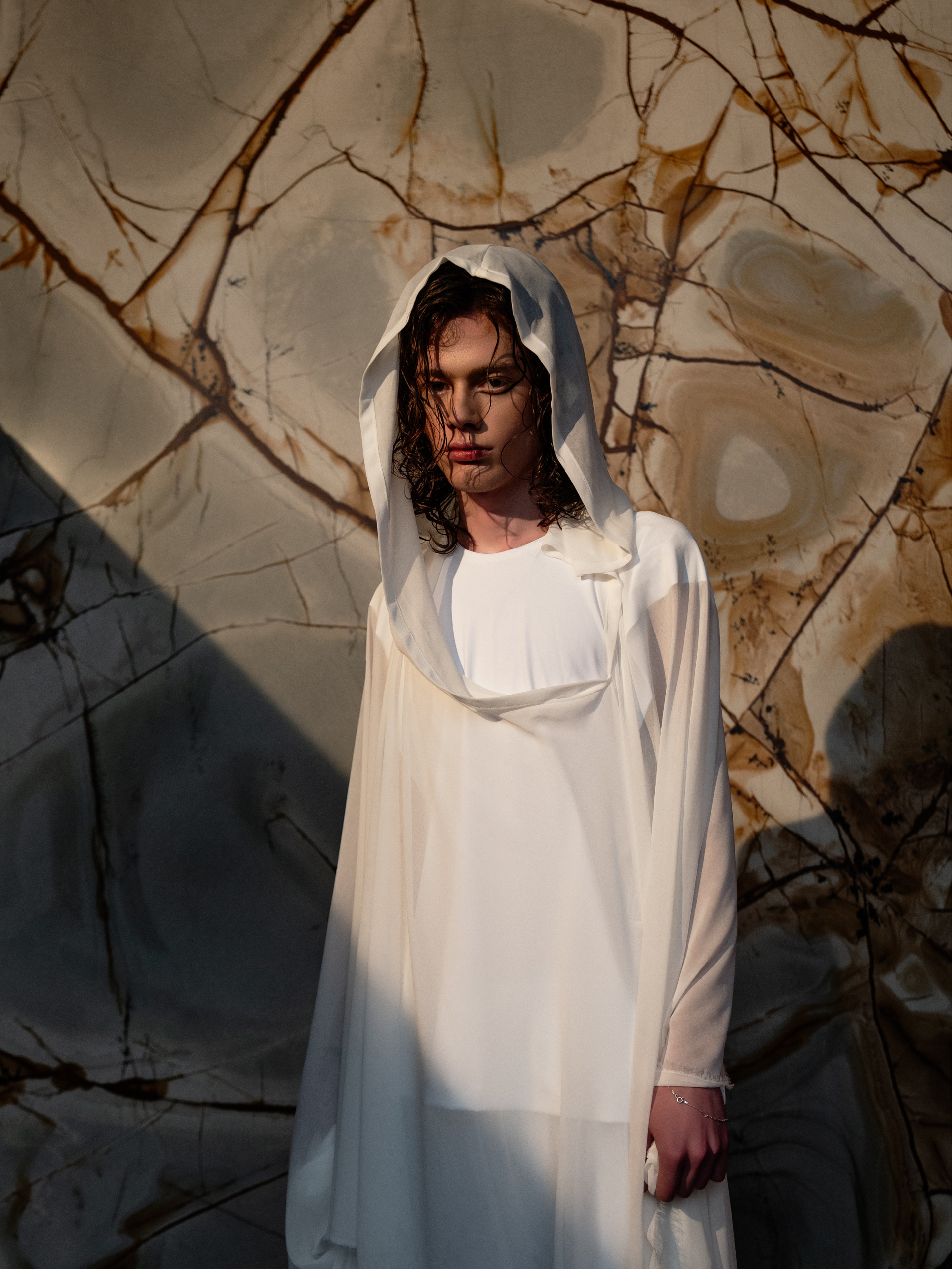 Italstone model in a white hooded gown against veined marble — Shot in Stone | BoldCrest