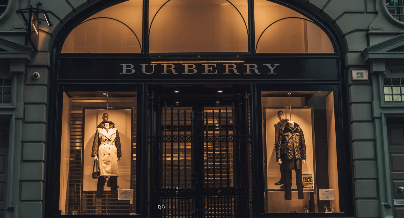 High-end Burberry store with black facade and gold-lit display windows showcasing designer jackets and trench coats
