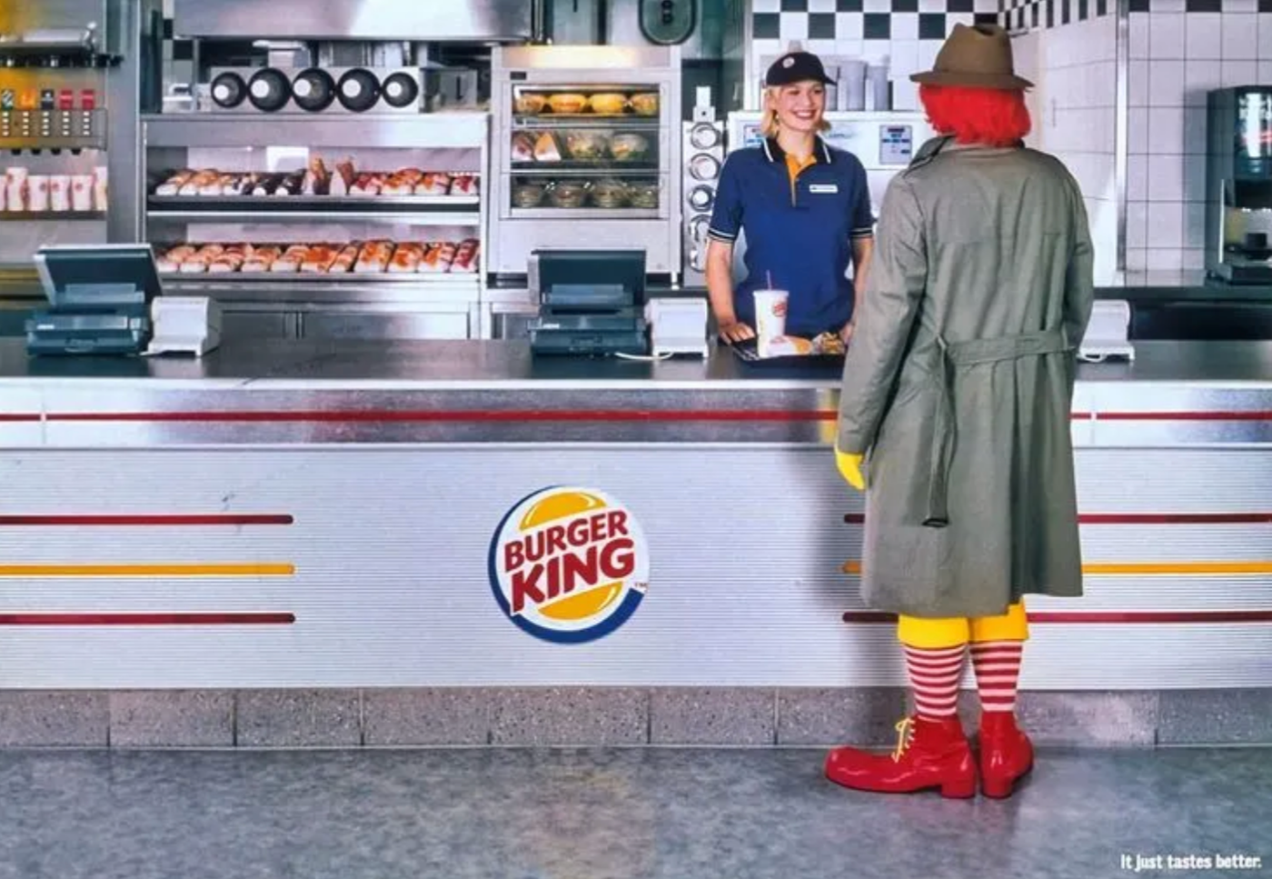 Ronald McDonald character in red and yellow outfit standing at Burger King counter with employee, tagline "It just tastes better"