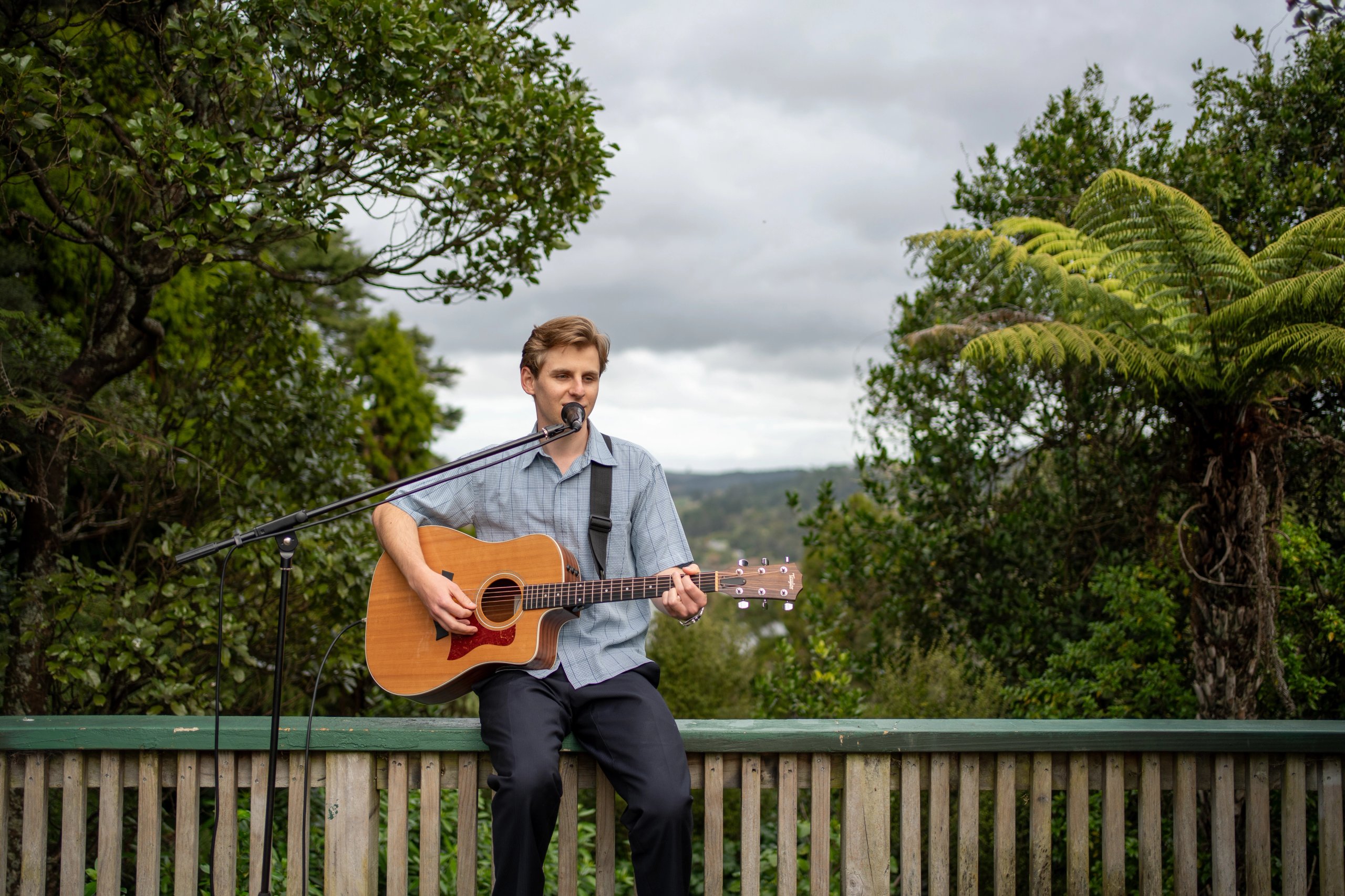 Niklas Meads sitting with an acoustic guitar and microphone with forest background