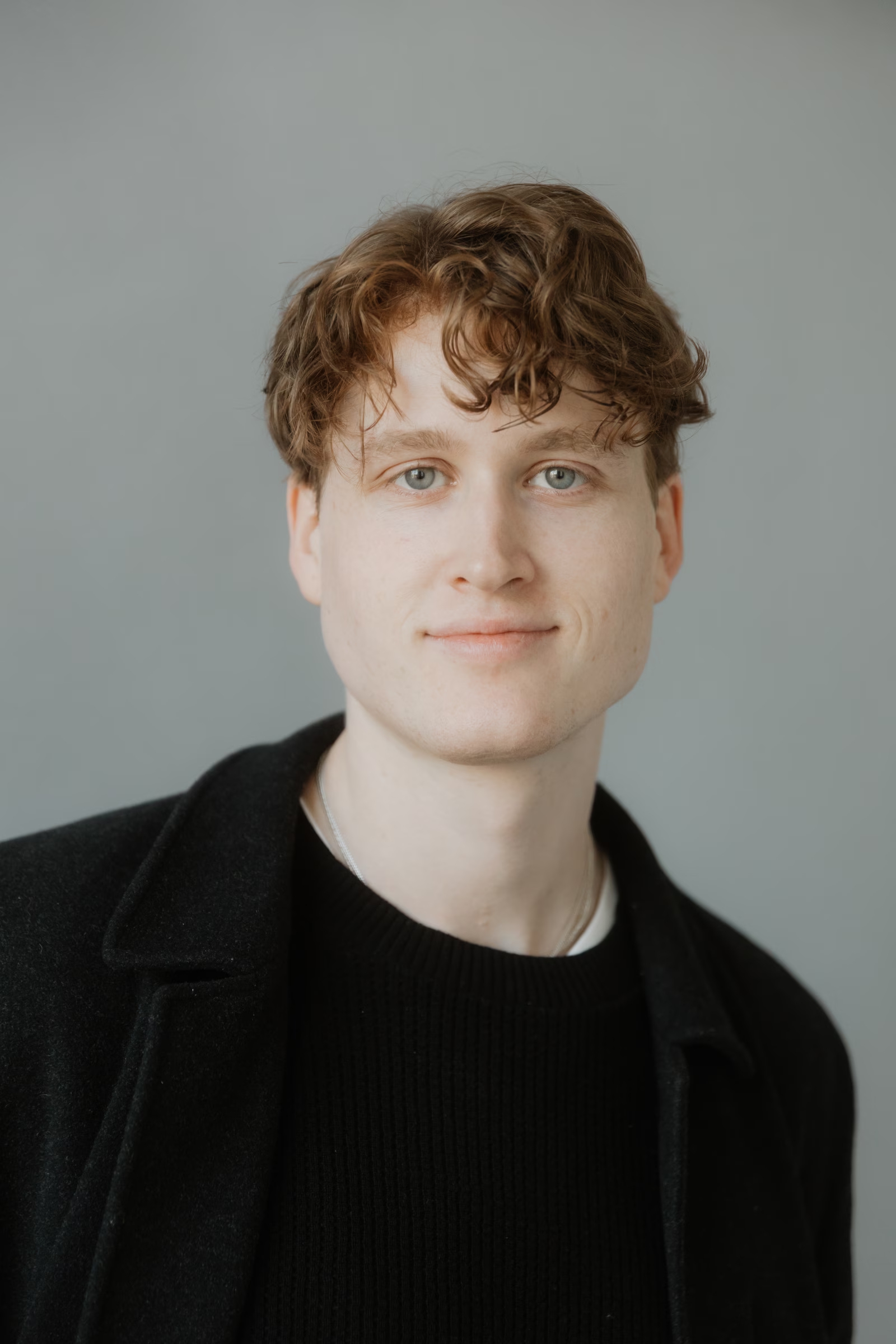 Close-up portrait of Julian wearing a dark top against a soft neutral background