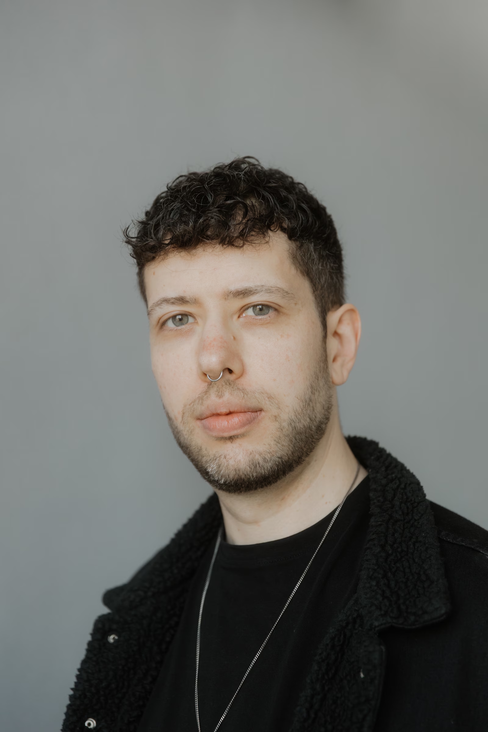 Close-up portrait of Adrian with short dark hair wearing a black jacket against a soft gray background