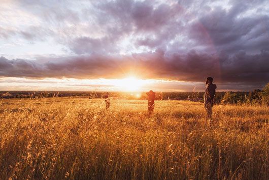 People standing in wheat field staring at sunset