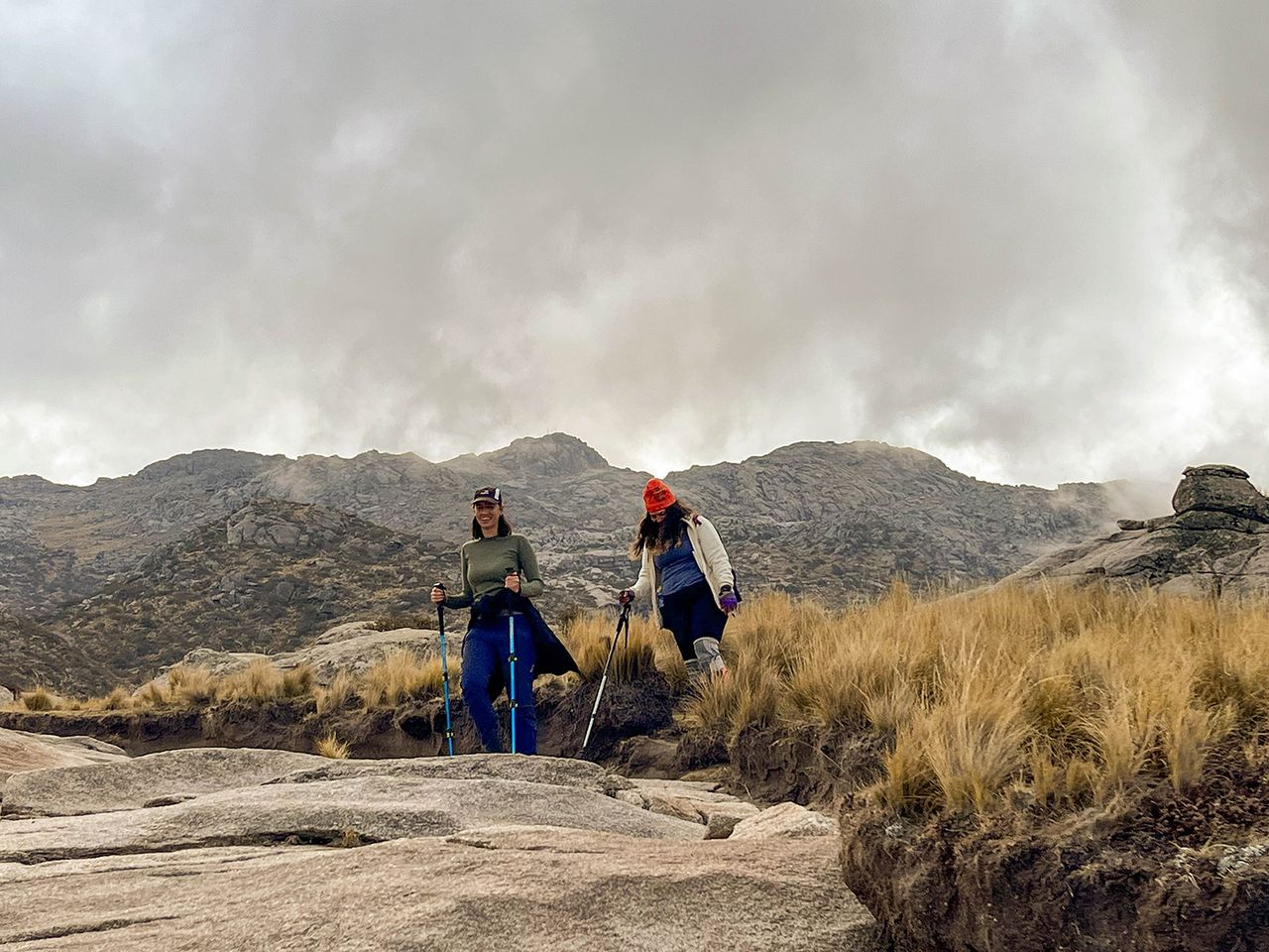 Senderistas caminando entre formaciones rocosas en Los Gigantes con las sierras de Córdoba al fondo
