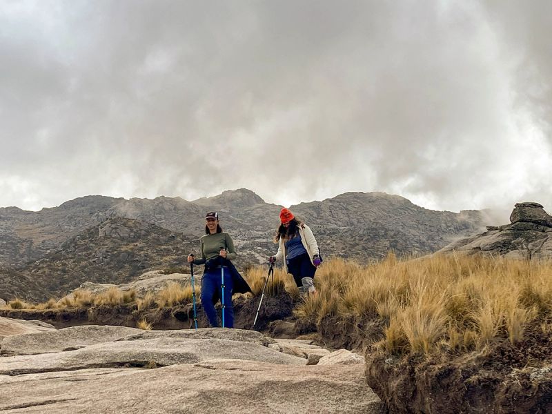 Senderistas caminando entre formaciones rocosas en Los Gigantes con las sierras de Córdoba al fondo