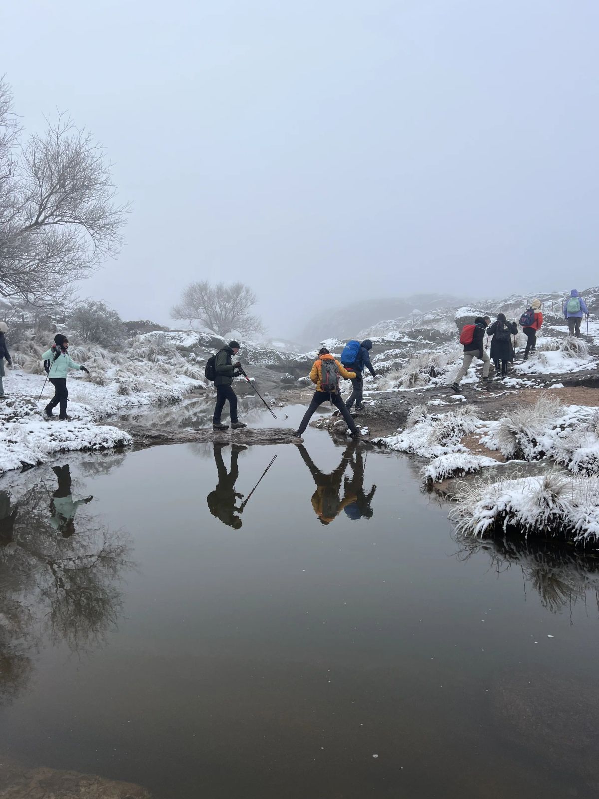 Trekkers reflejados en una laguna rodeada de nieve en las Sierras Grandes