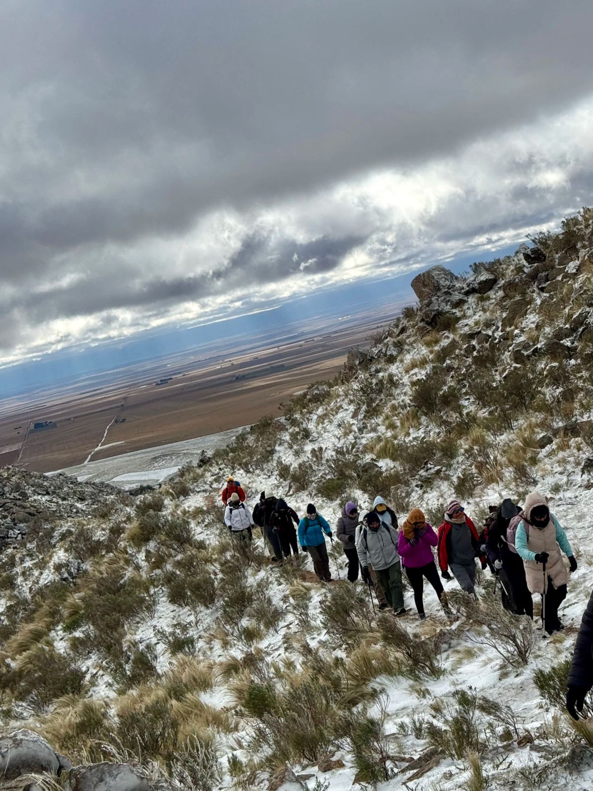 Columna de trekkers ascendiendo por la ladera nevada con el horizonte puntano al fondo