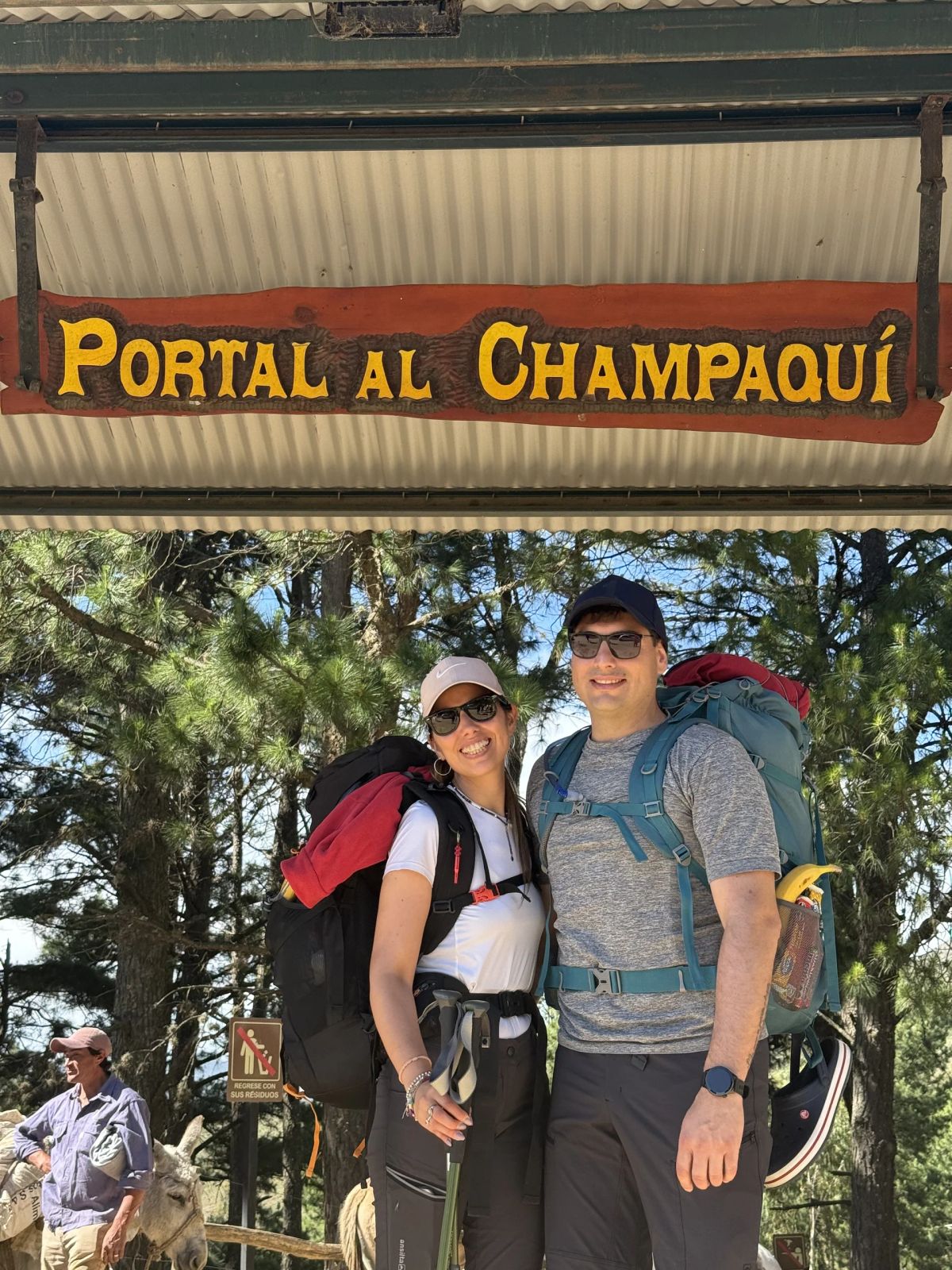 Pareja de participantes con mochilas de expedición bajo el cartel del Portal al Champaquí