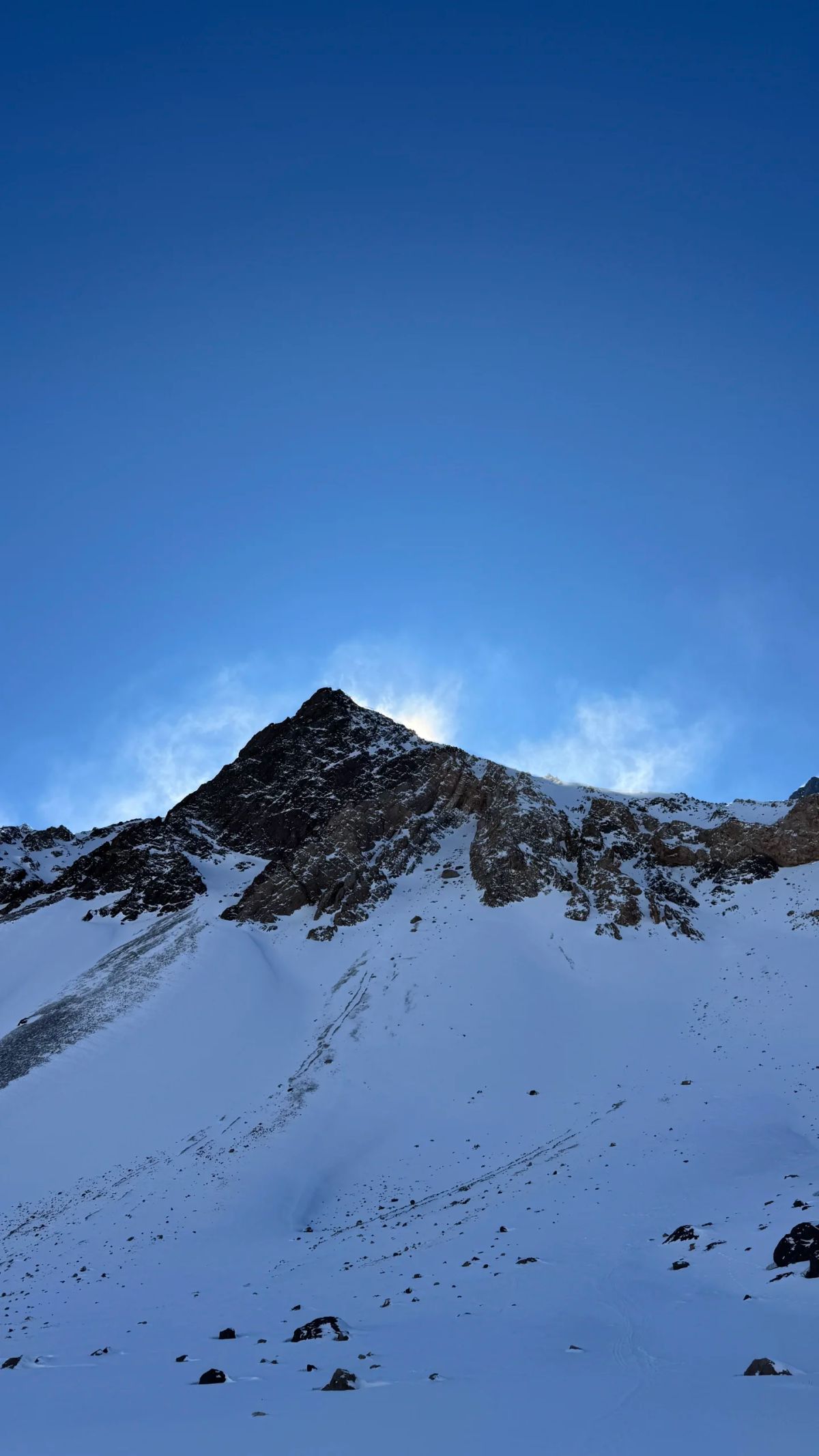 El sol asomando detrás de una cumbre nevada de la Cordillera de los Andes en Mendoza durante el ascenso