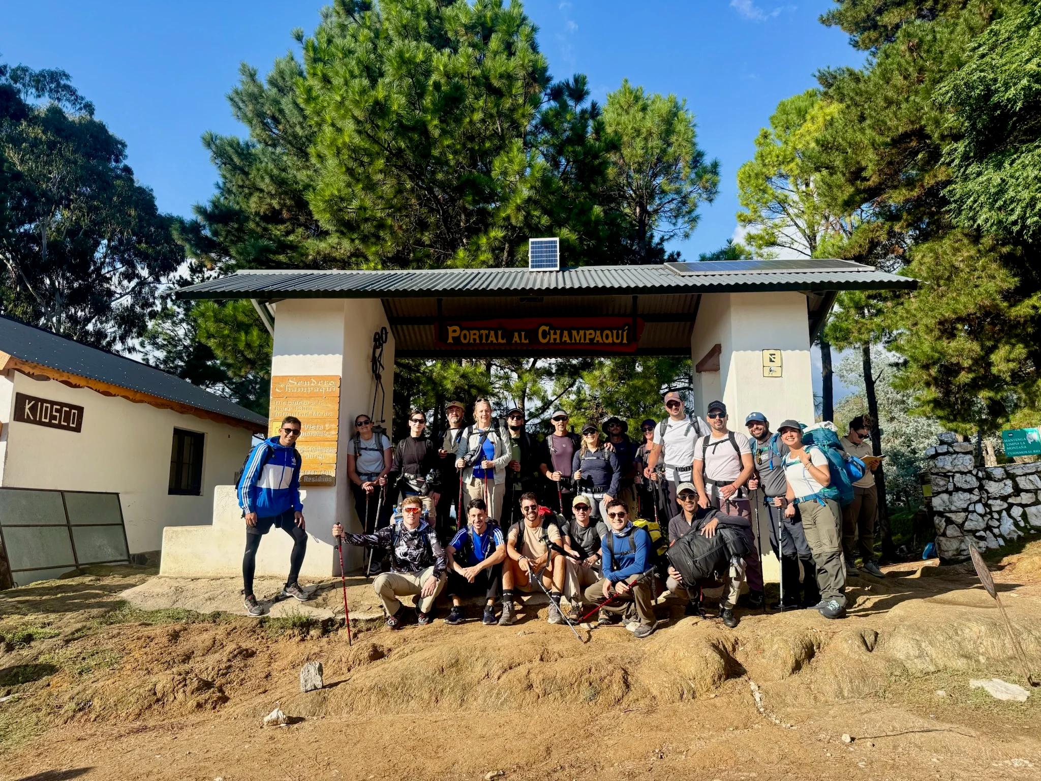 Grupo completo de la Salida 202 de Mons posando bajo el arco del Portal al Champaquí, en Villa Alpina, antes de comenzar el trekking
