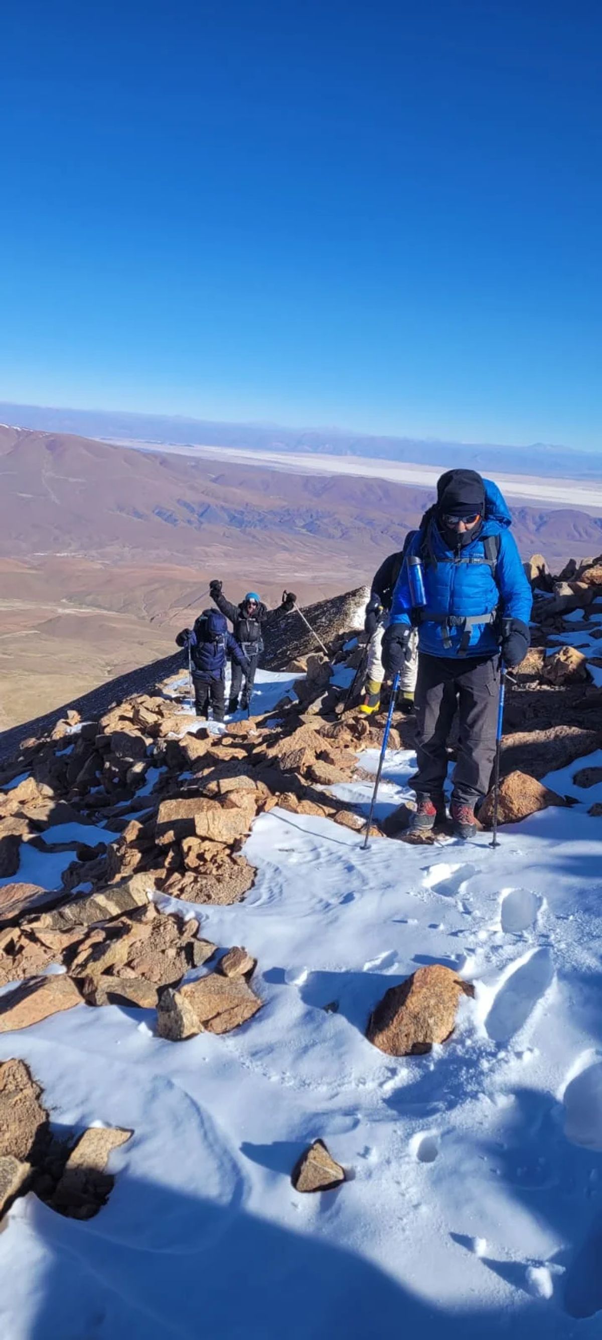 Montañista ascendiendo sobre la nieve bajo el cielo azul profundo de la alta puna de Jujuy