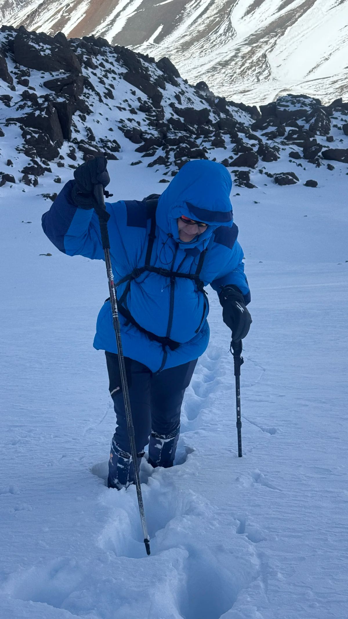 Montañista con campera de pluma azul abriendo huella en nieve profunda camino a los 4.000 metros