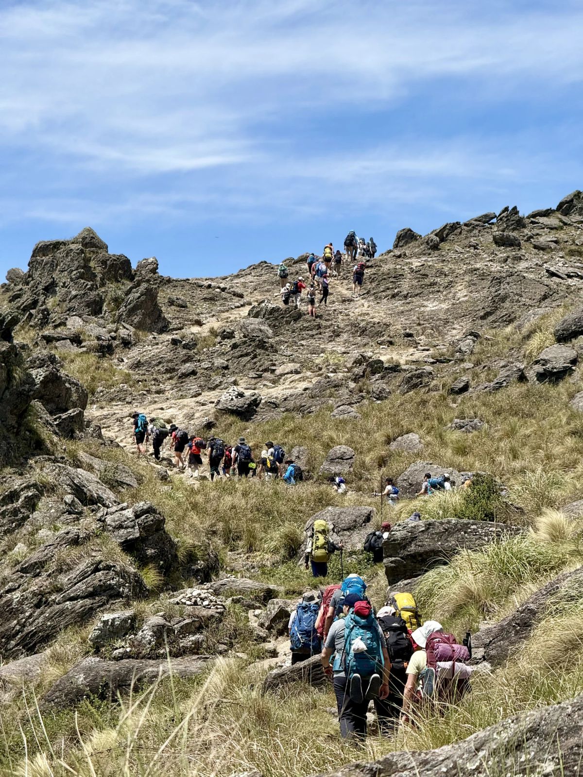 Columna de trekkers subiendo por el sendero rocoso de las Sierras Grandes de Córdoba