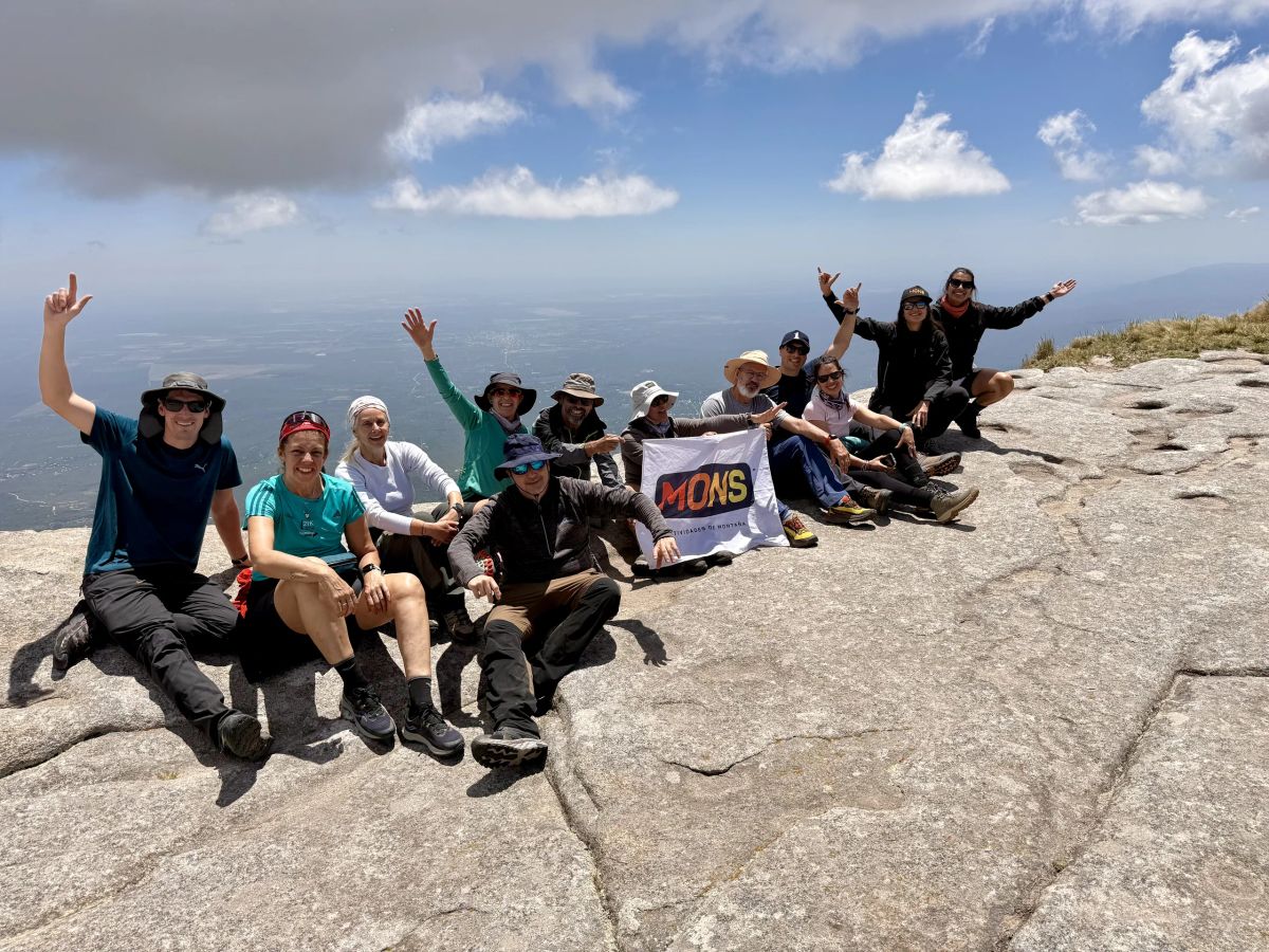 Festejo del contingente completo con la bandera de Mons sobre el granito de la cumbre