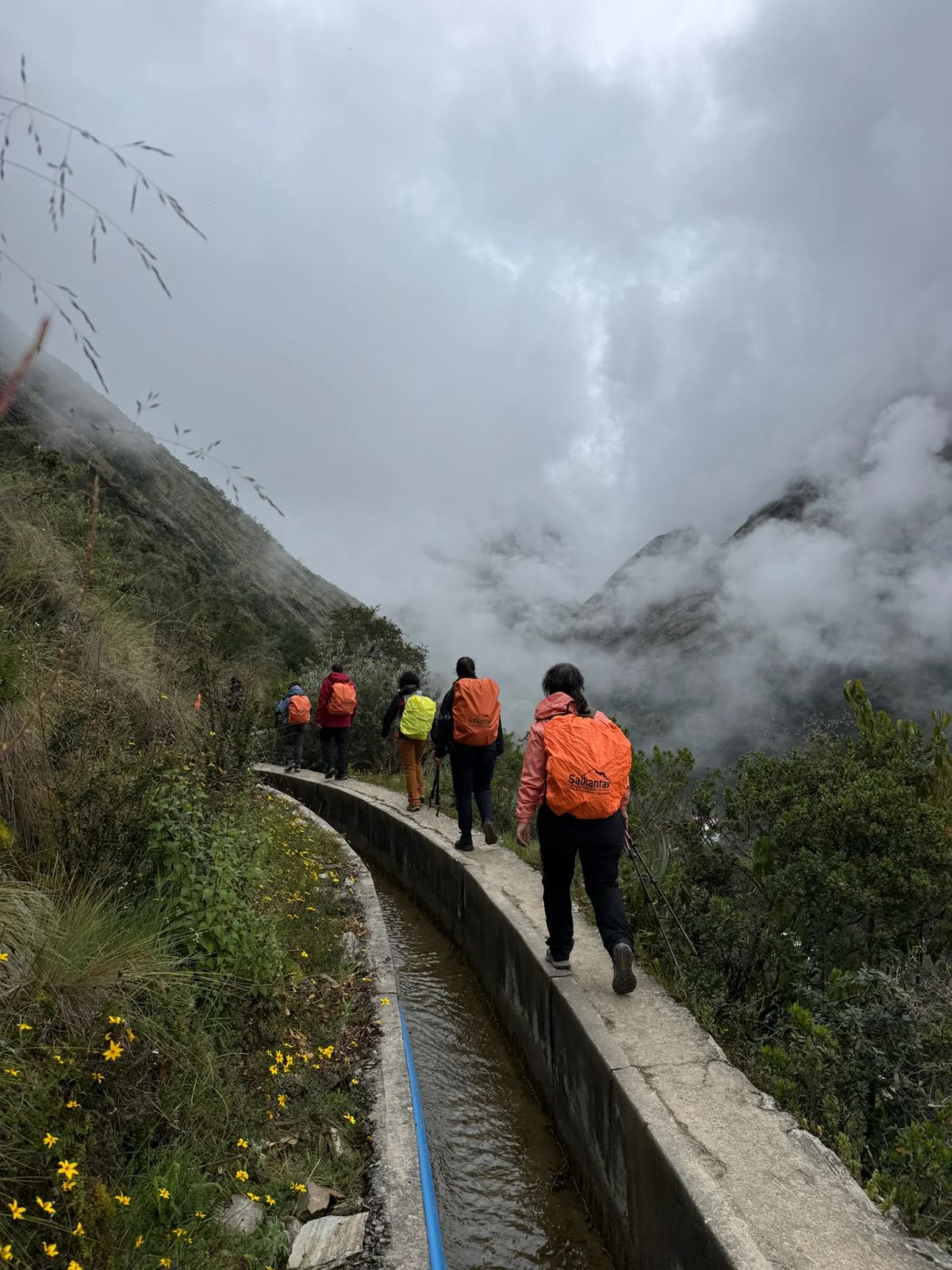 Fila de trekkers junto al canal entre las nubes de la cordillera de Vilcabamba