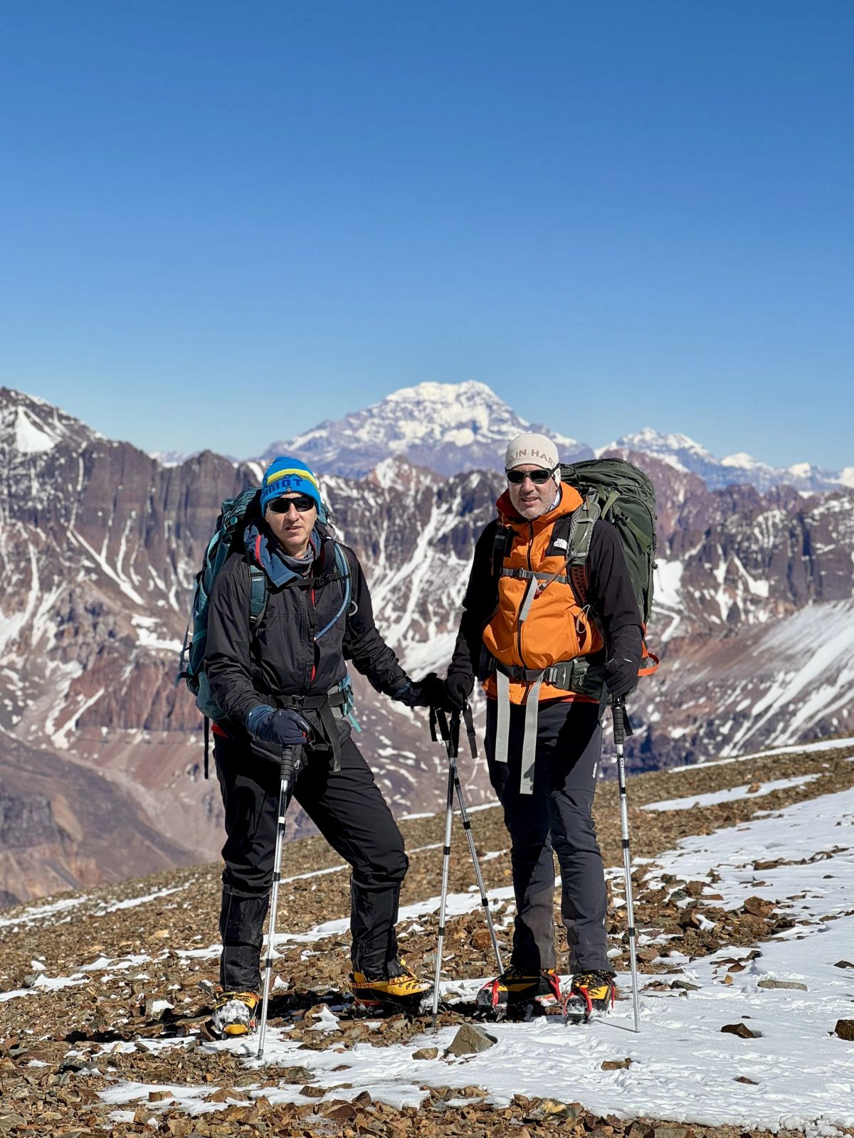 Dos andinistas de Mons dándose la mano con la mole del Cerro El Plata detrás