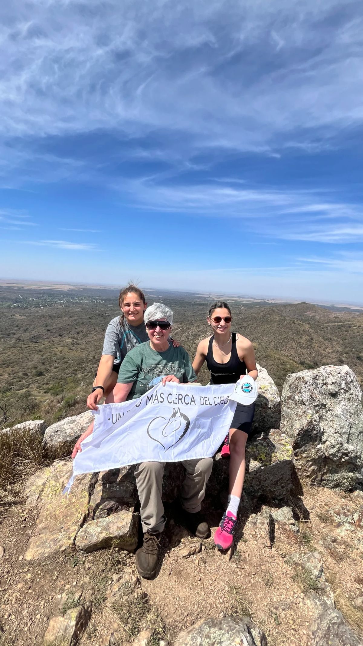 Trekkers posando con una bandera sobre las rocas de la cumbre con la llanura cordobesa al fondo