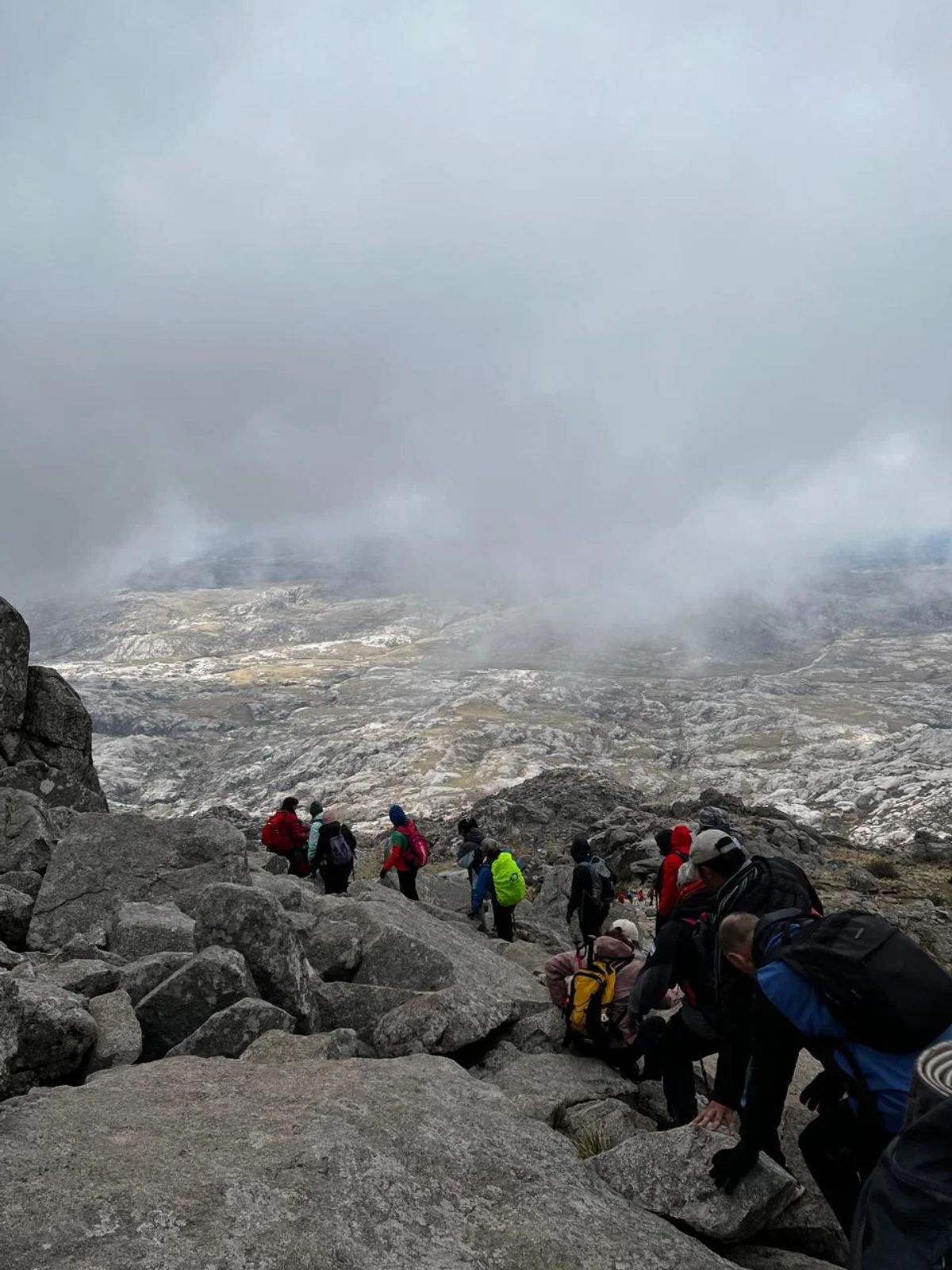 Trekkers subiendo entre las rocas con la niebla cubriendo la ladera del Champaquí