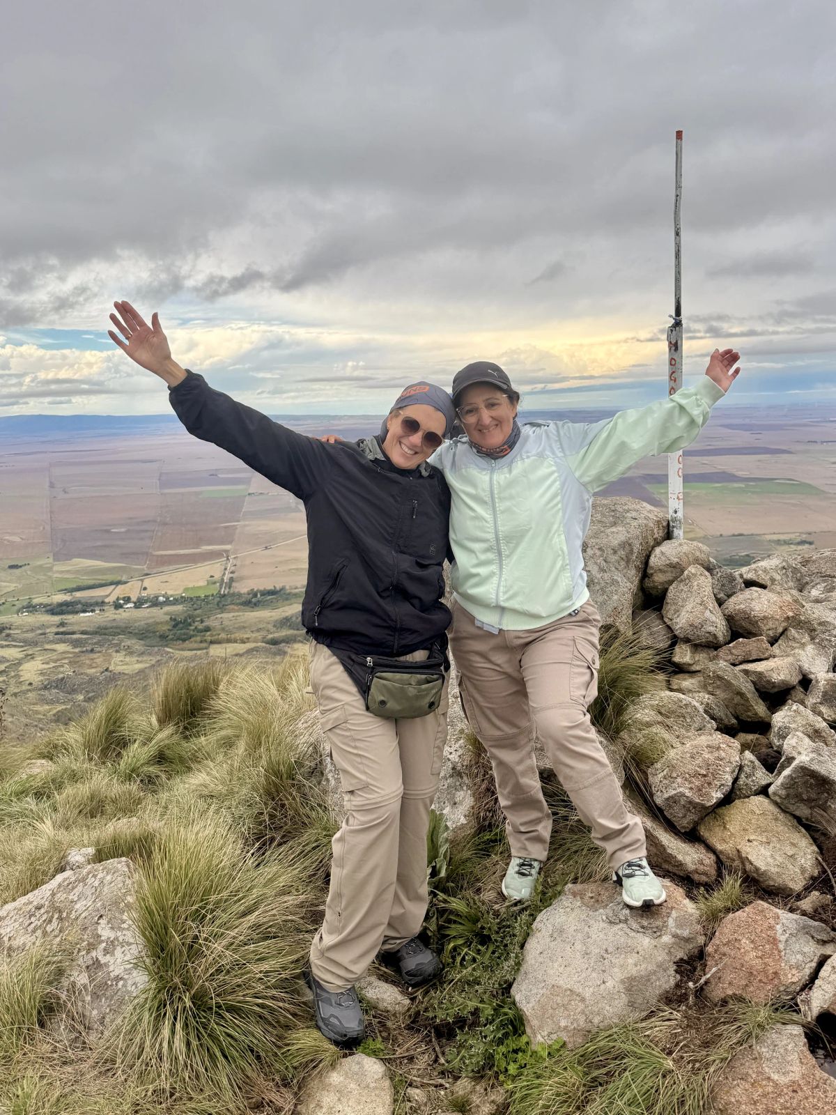 Dos trekkers junto al mástil de la cumbre del Cerro El Morro, San Luis